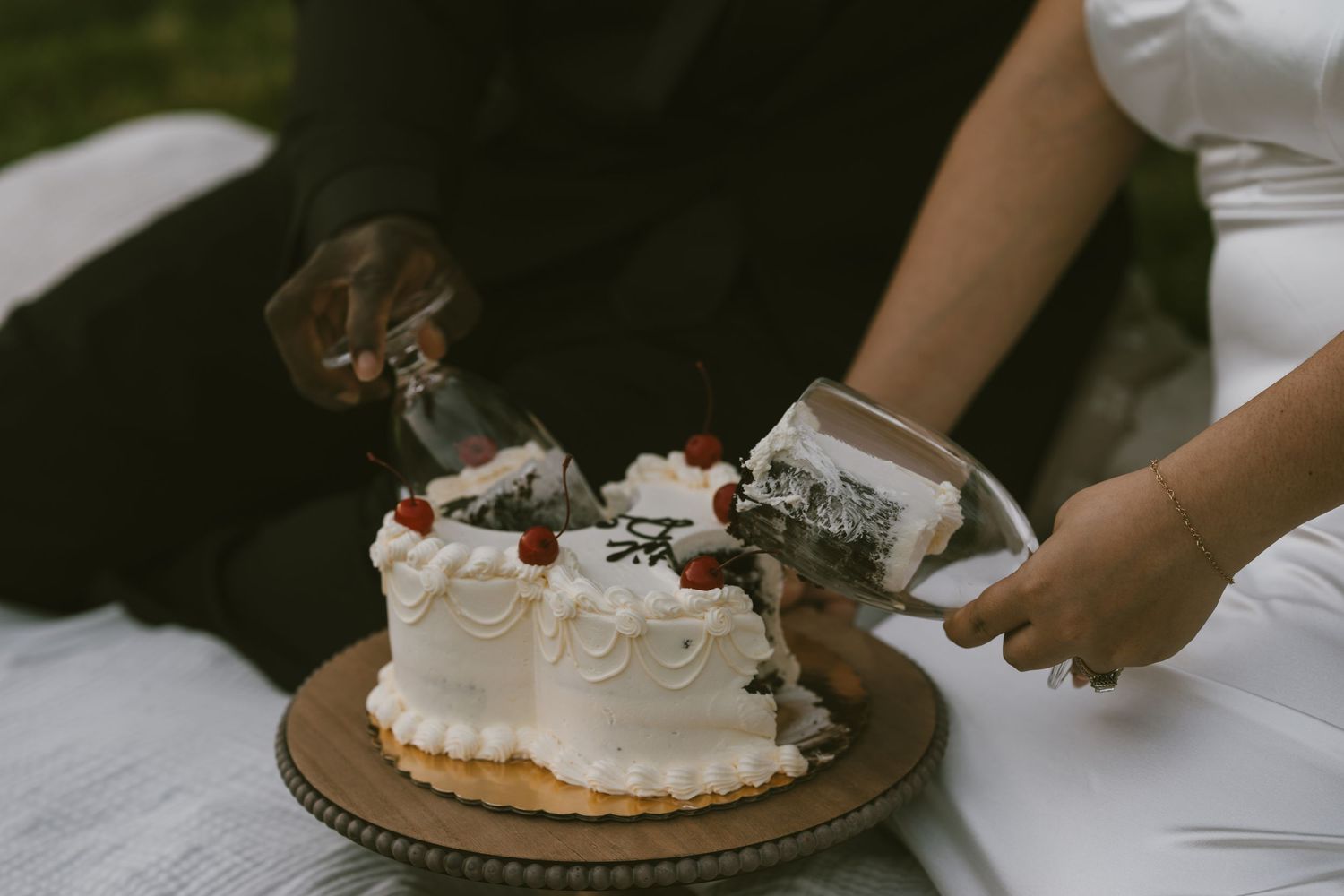 A person cuts into a white frosted cake decorated with swirls and topped with chocolate ornaments on a bronze platter.