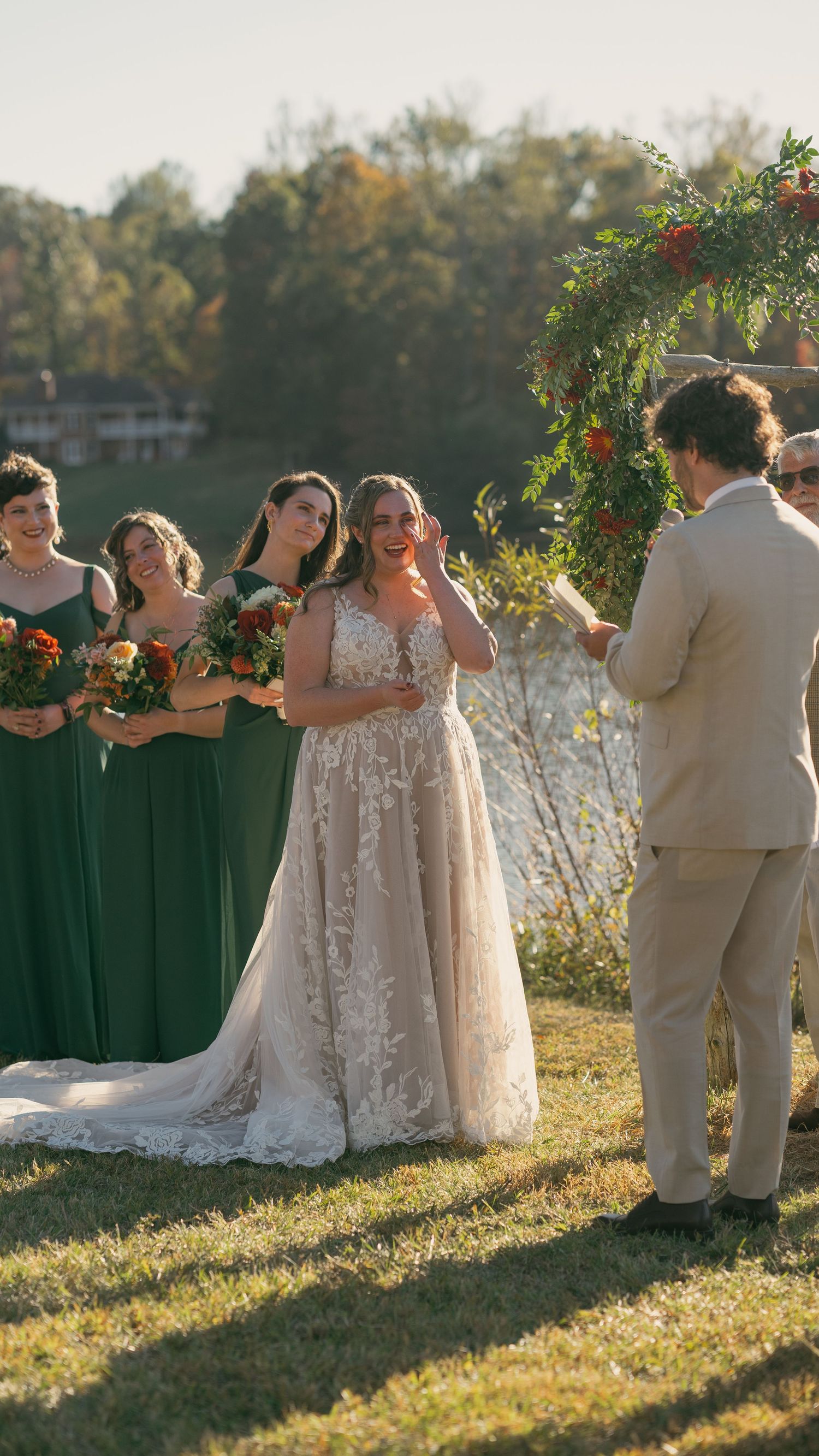 Wedding party in green dresses and khaki suits poses in a sunlit field.