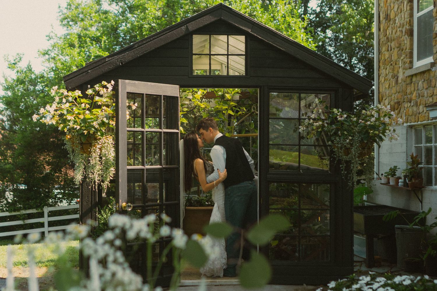Romantic greenhouse wedding photo with couple silhouetted against garden windows.