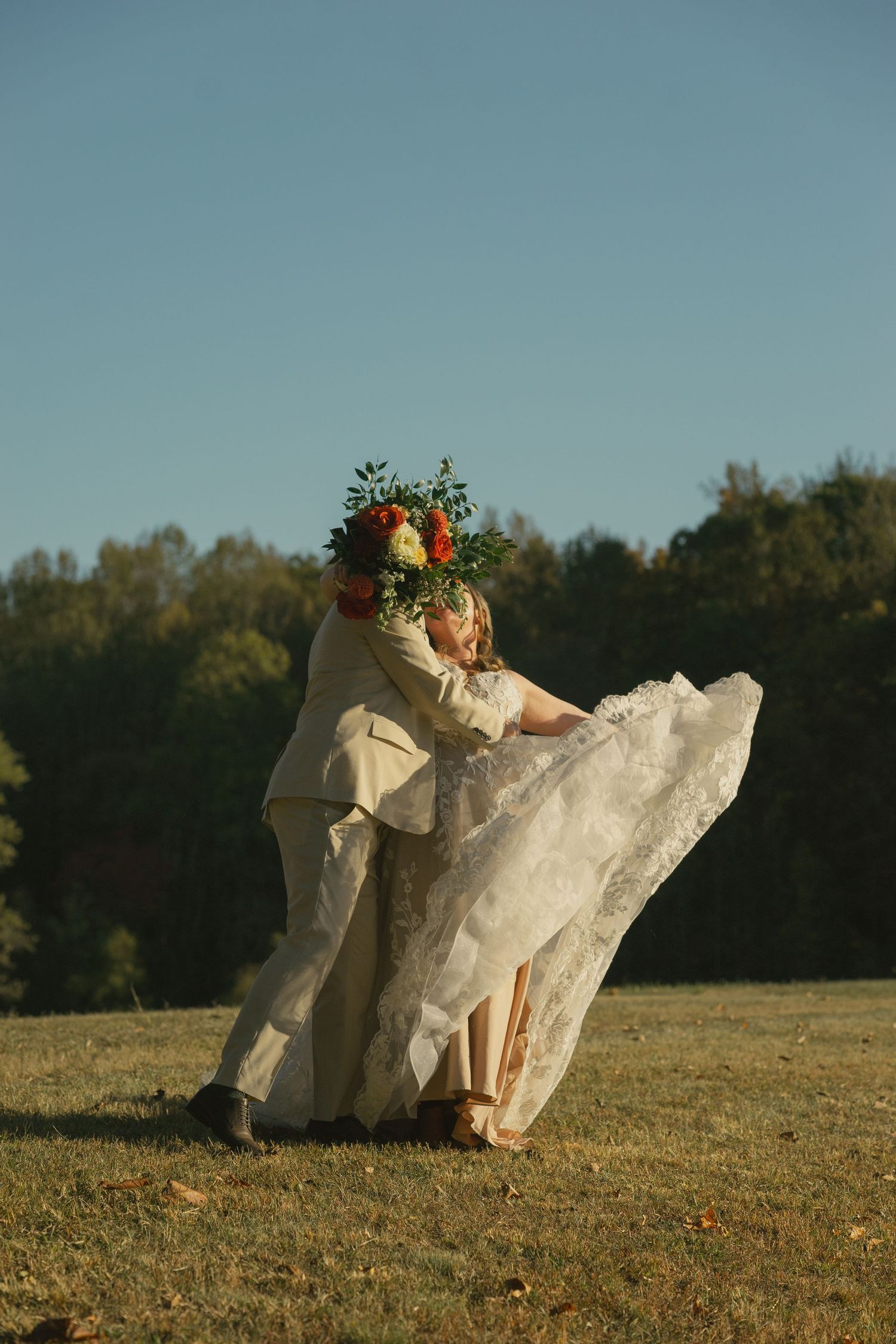 Couple dancing in field at sunset with flowing white dress and autumn backdrop.