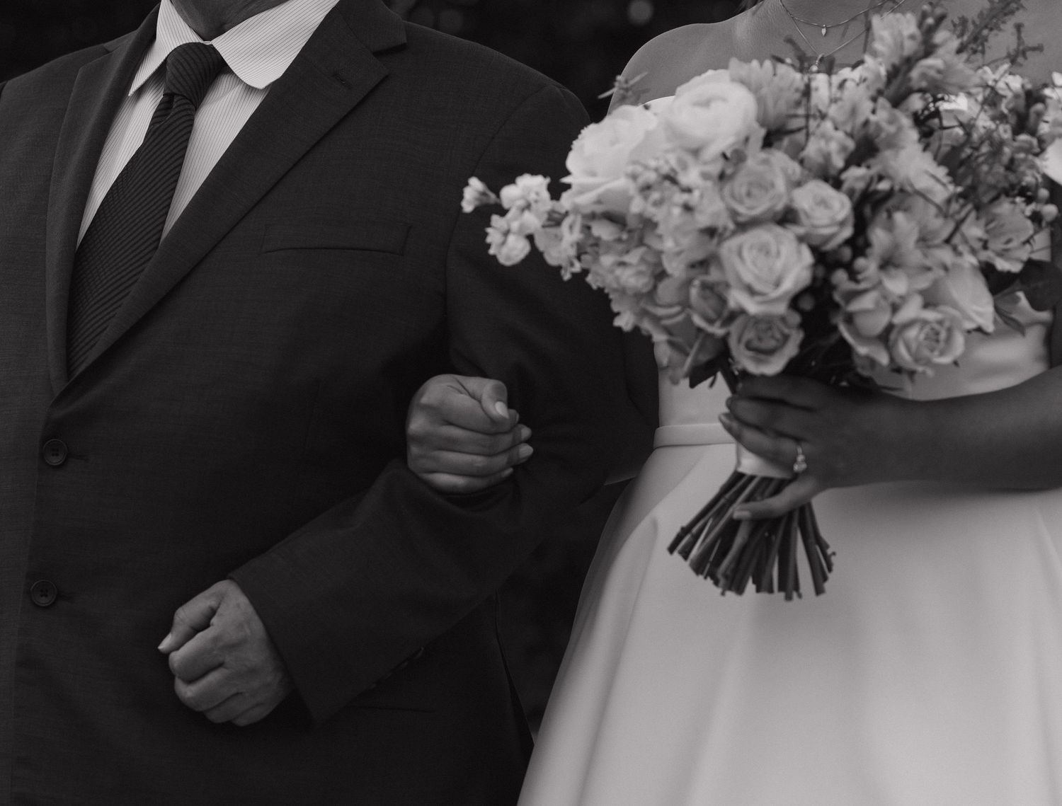 Wedding party members holding elegant white floral bouquets against dark formal attire.