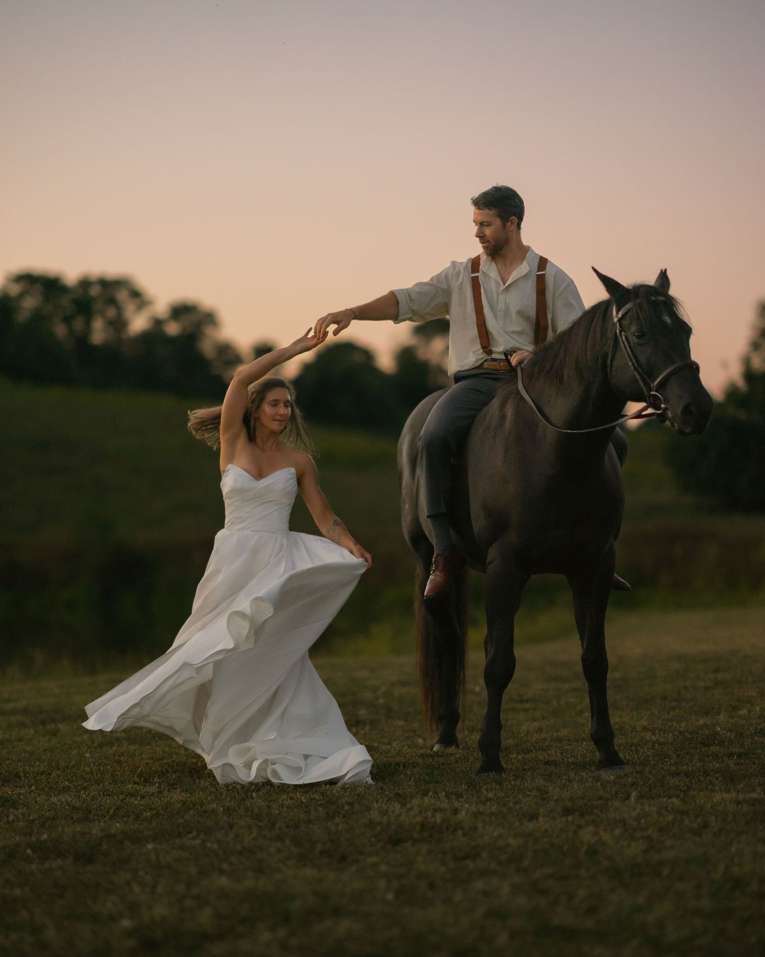 A new Bride twirling around in her wedding dress while the Groom admires her from atop his horse.