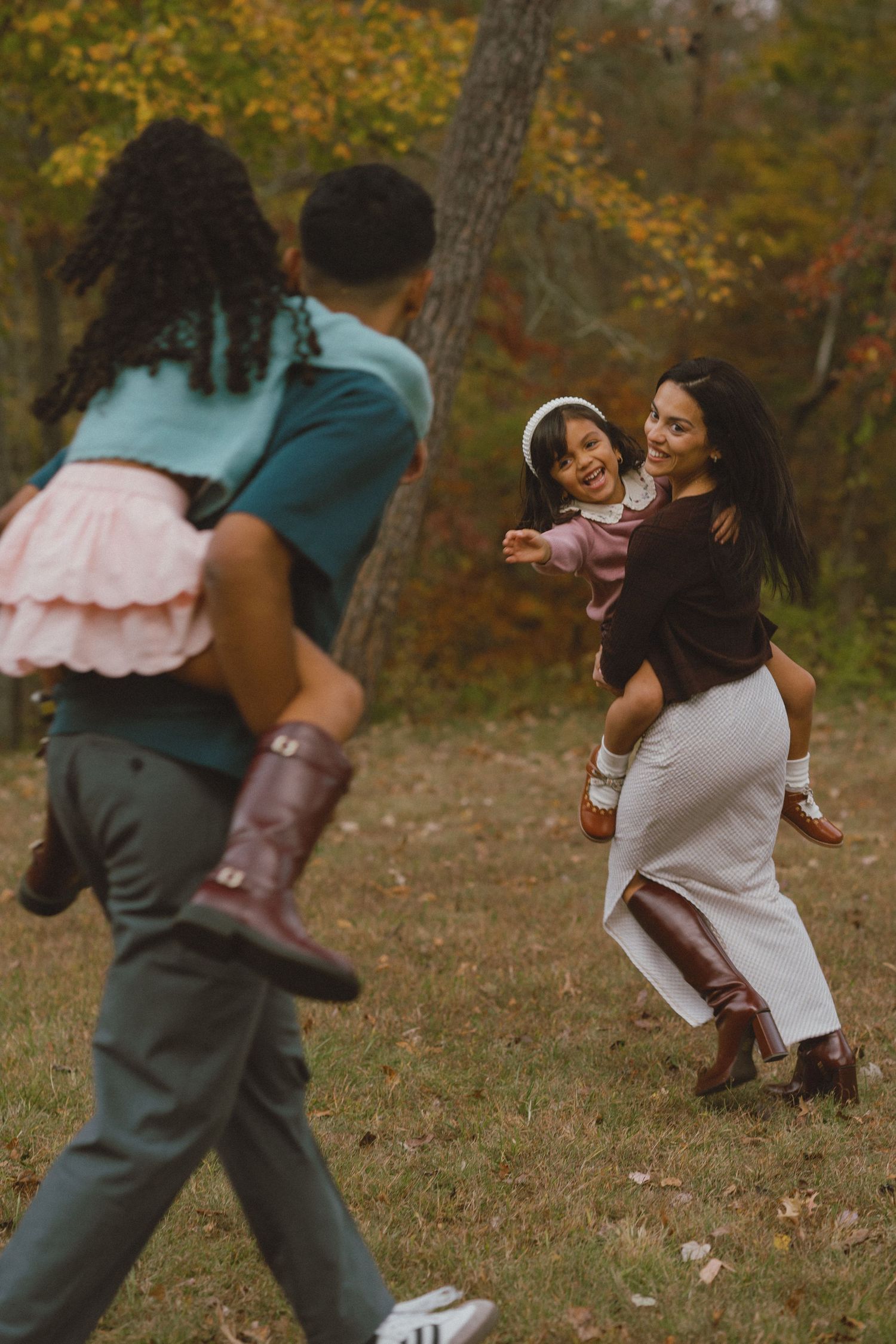 A couple dances playfully together in an autumn setting with fallen leaves and trees in the background.