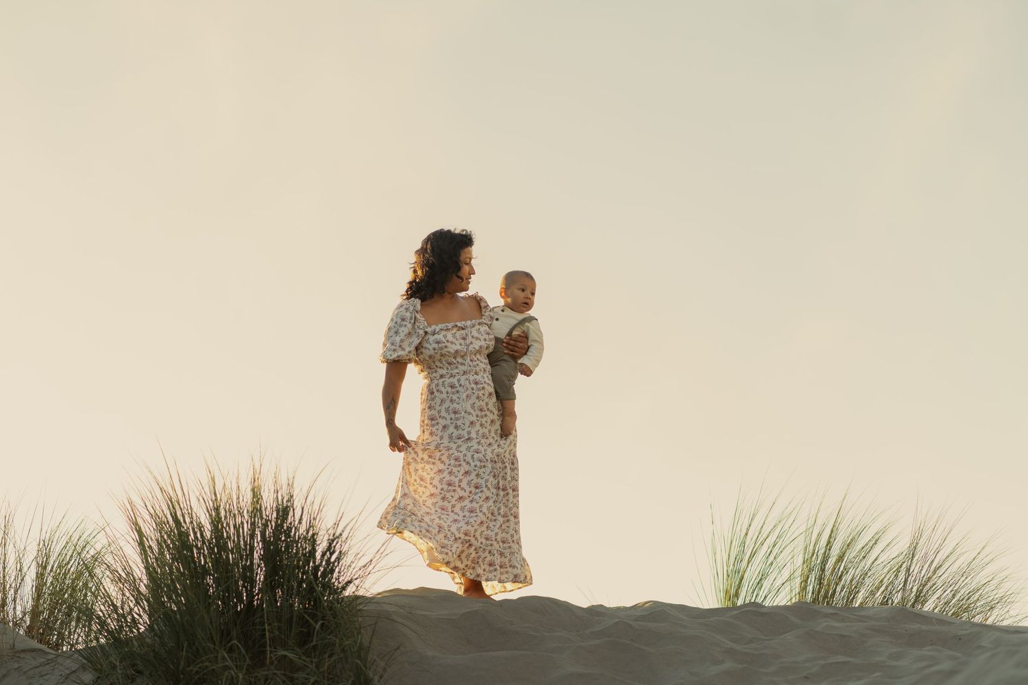 Silhouette of two figures standing on a sand dune at sunset with flowing dress and grasses. Dillon Beach, California.