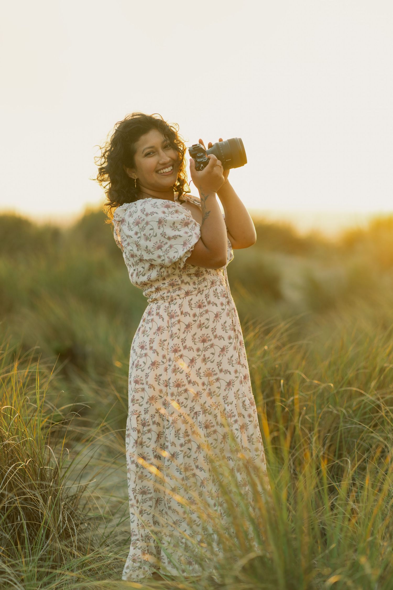 Photographer basking in the golden hour sunlight at Dillon Beach, CA, holding up her Sony A7ii full frame camera with a Sony 85mm GM lens
