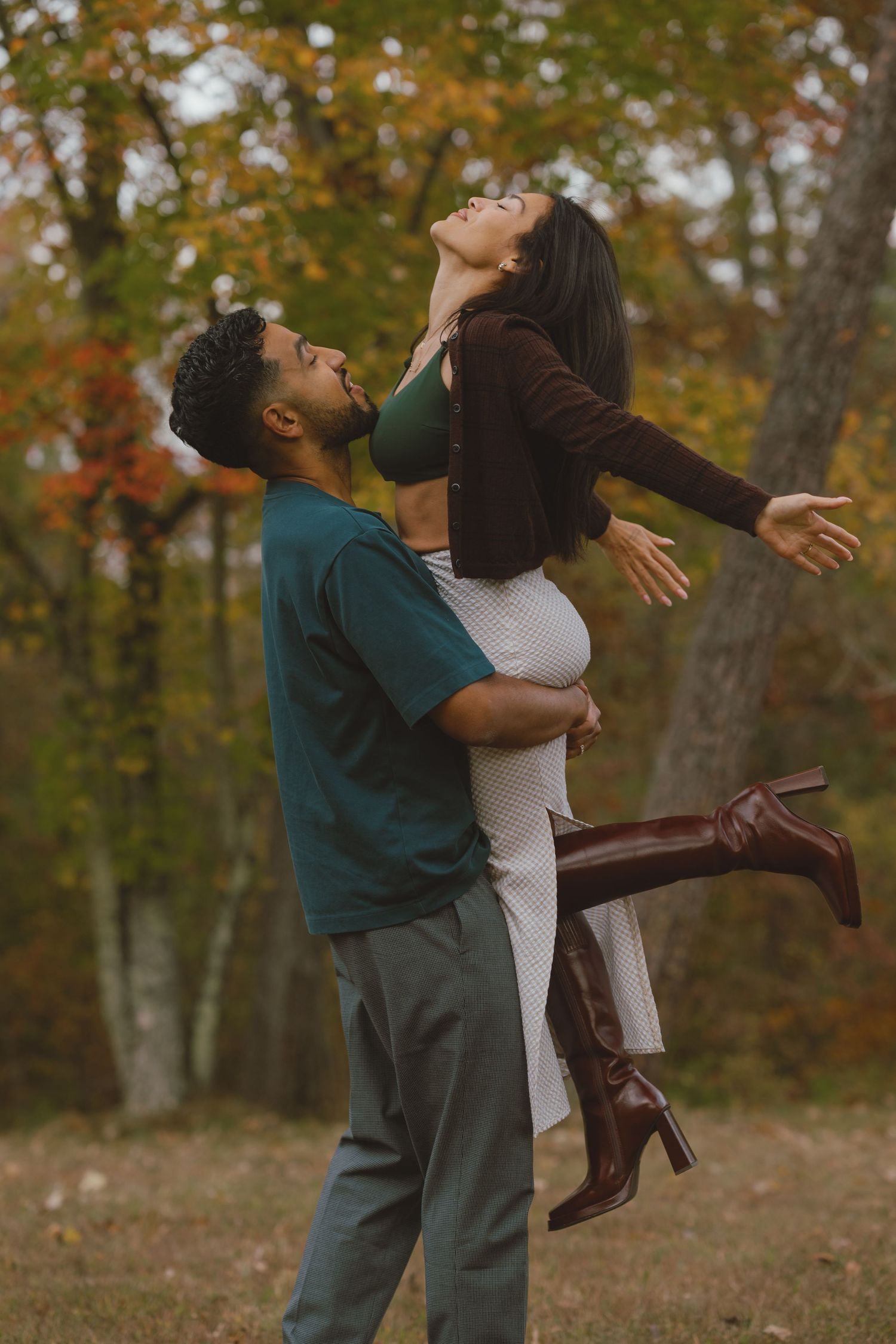 A couple embraces joyfully in a fall forest setting with autumn leaves in the background.
