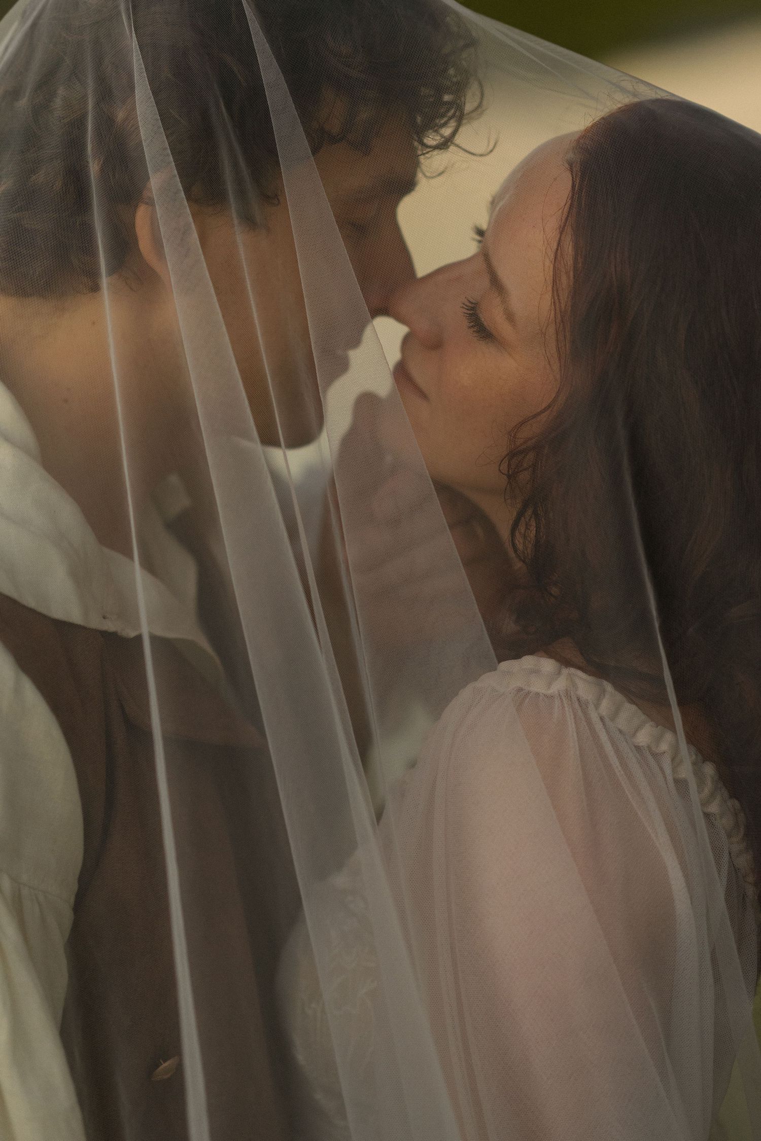 A romantic couple shares an intimate moment under a flowing white veil during their wedding photoshoot.