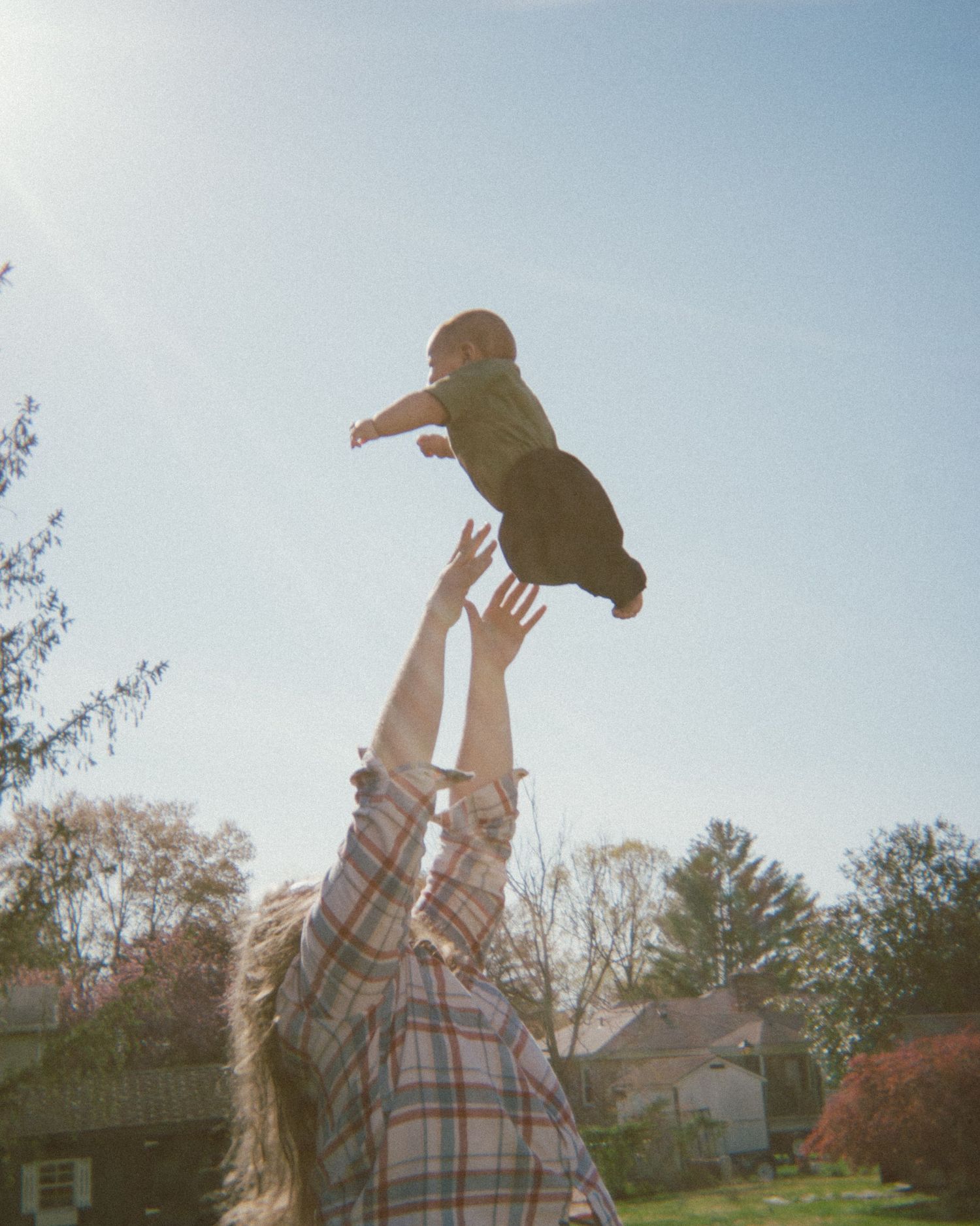 A child is joyfully tossed into the air against a bright sky in a backyard setting.