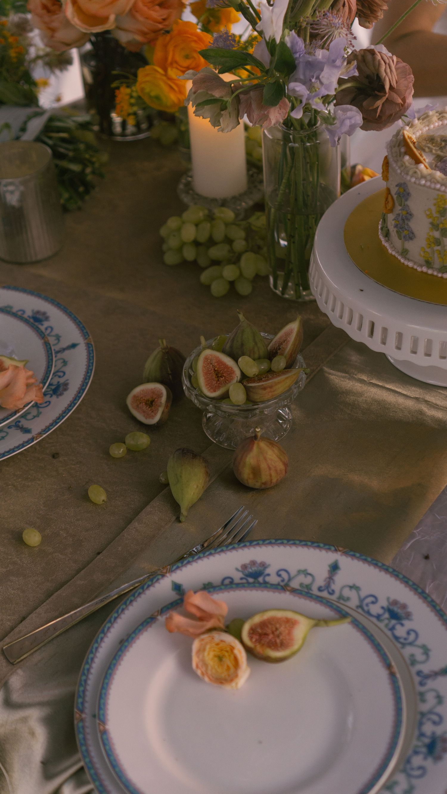 Elegant place settings with blue and white china plates adorned with fresh figs and grapes on a rustic wooden table.