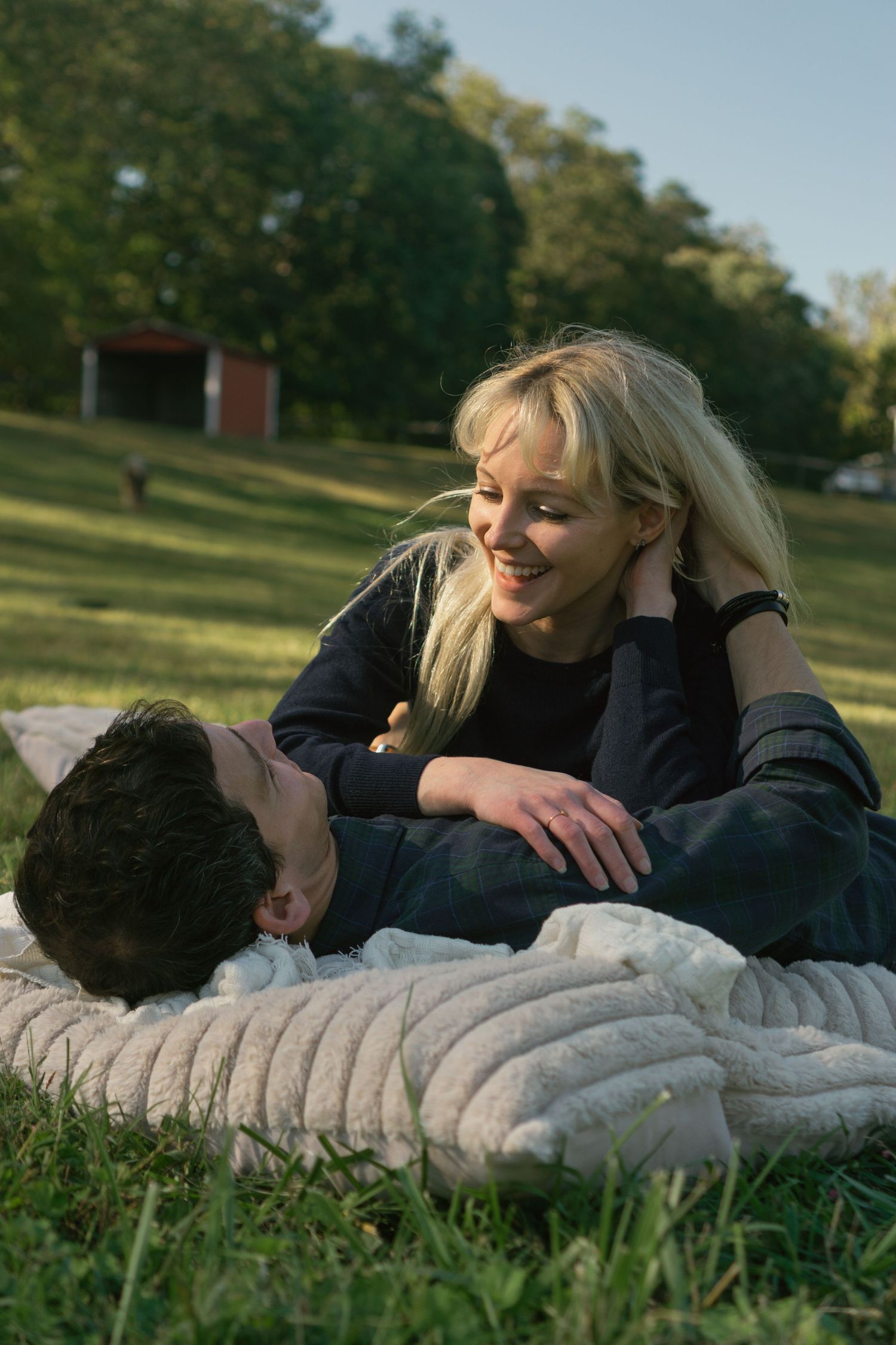 Two people lay together on a blanket in a grassy field during golden hour.