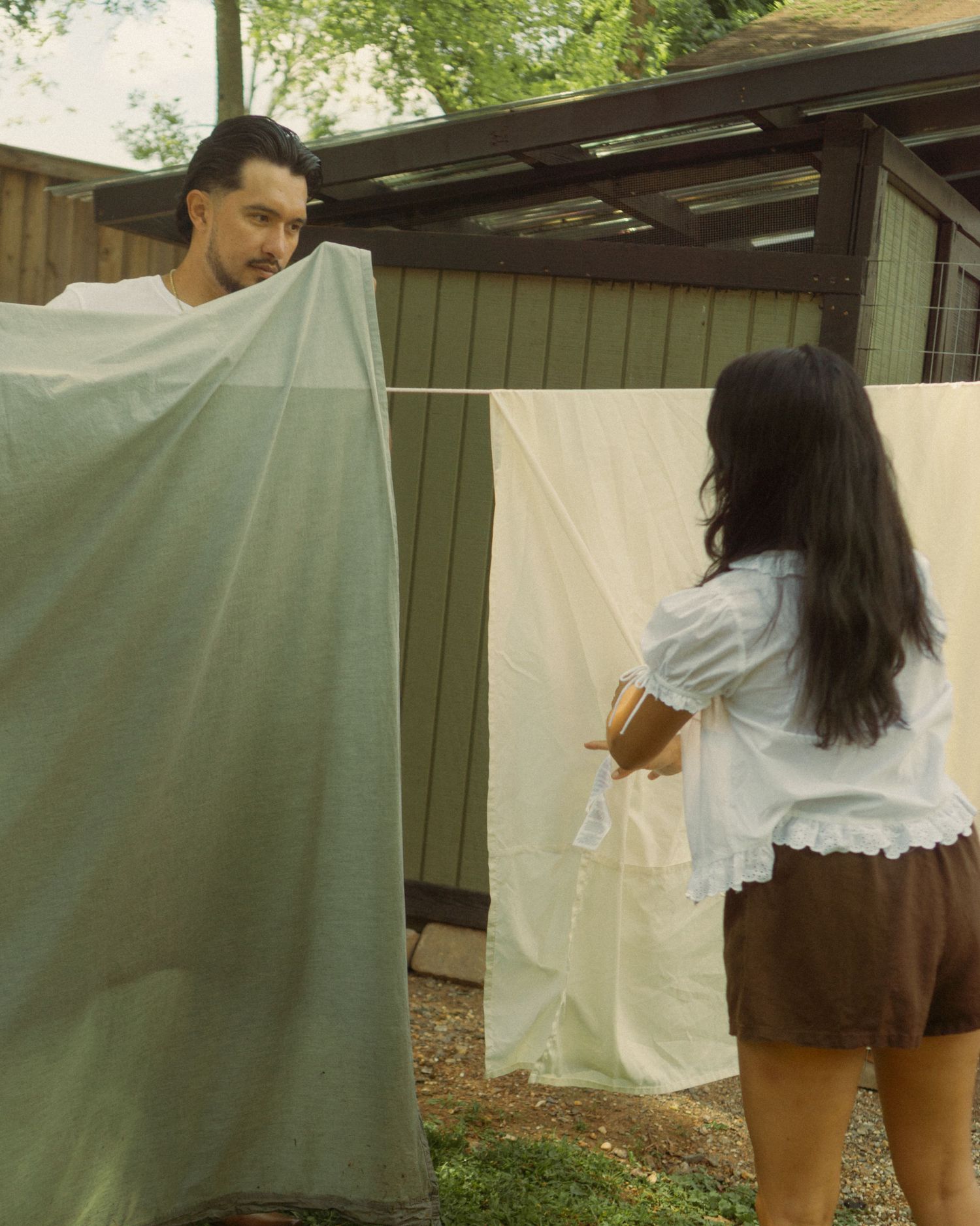 A sequence showing someone hanging white fabric on a clothesline outdoors.