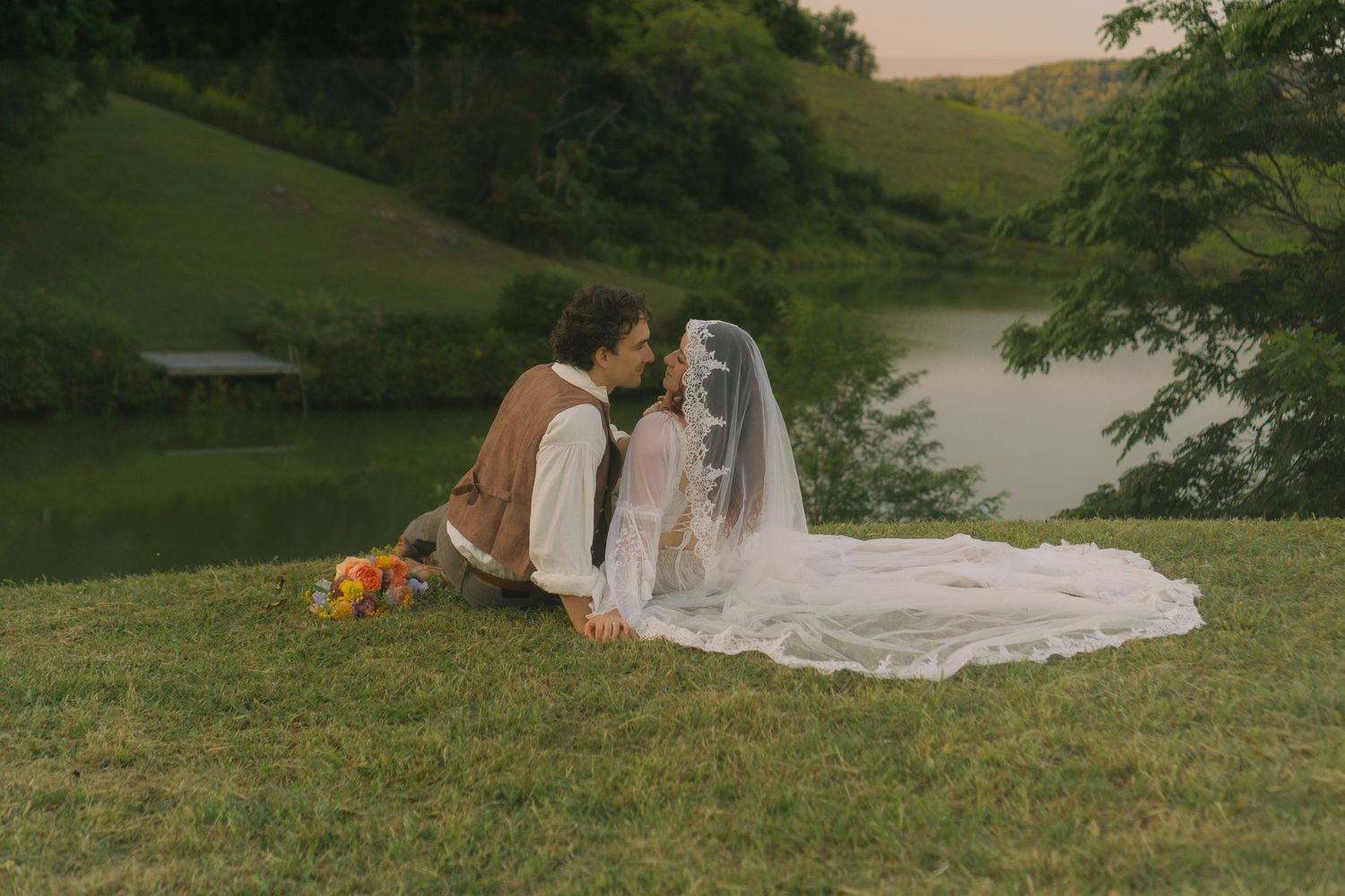 Couple lounging on grass during sunset with flowing white dress spread across the ground.