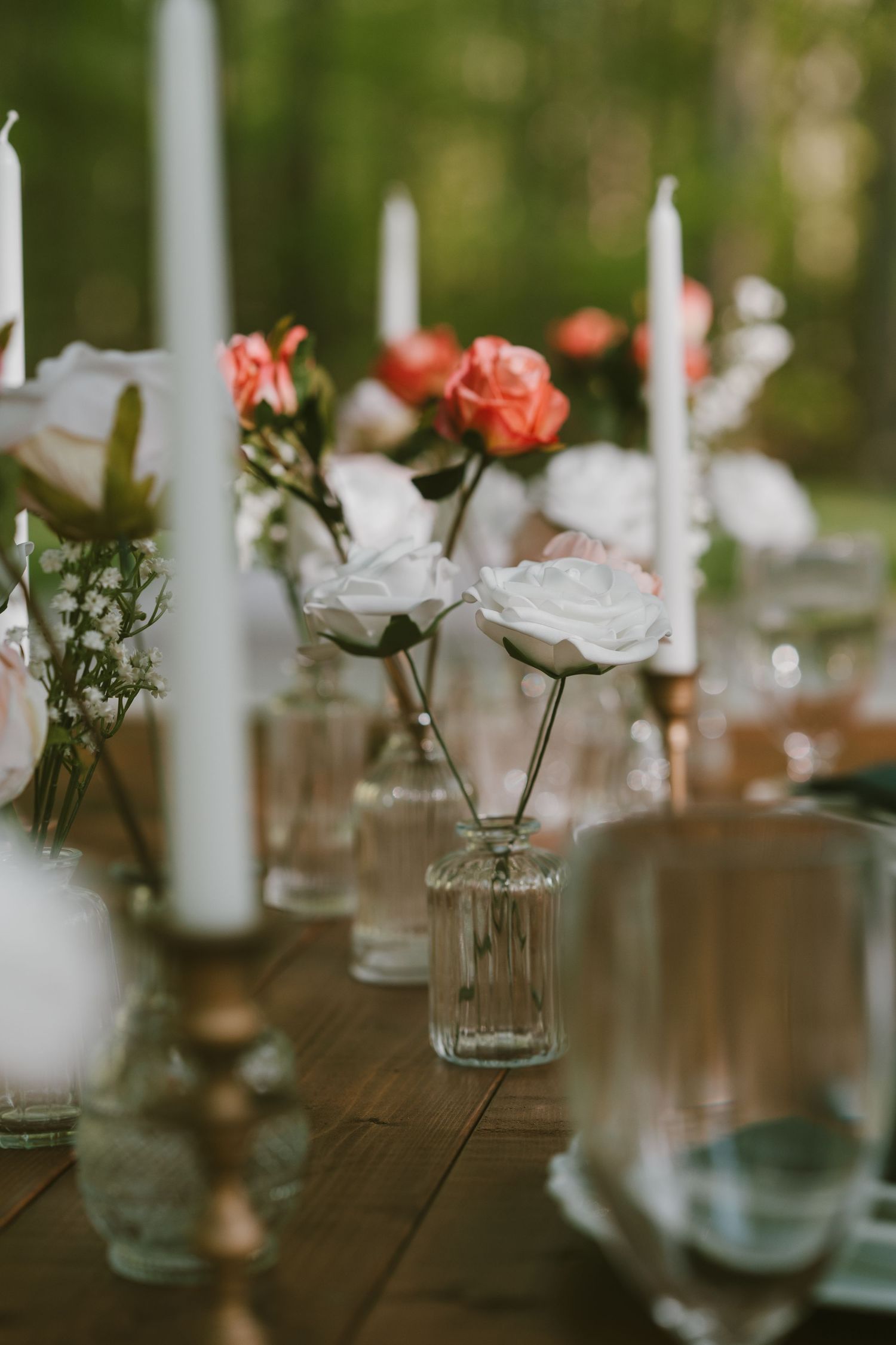wedding table adorned with white taper candles on copper candlestick holders, white and peach flowers in vintage clear glass vases