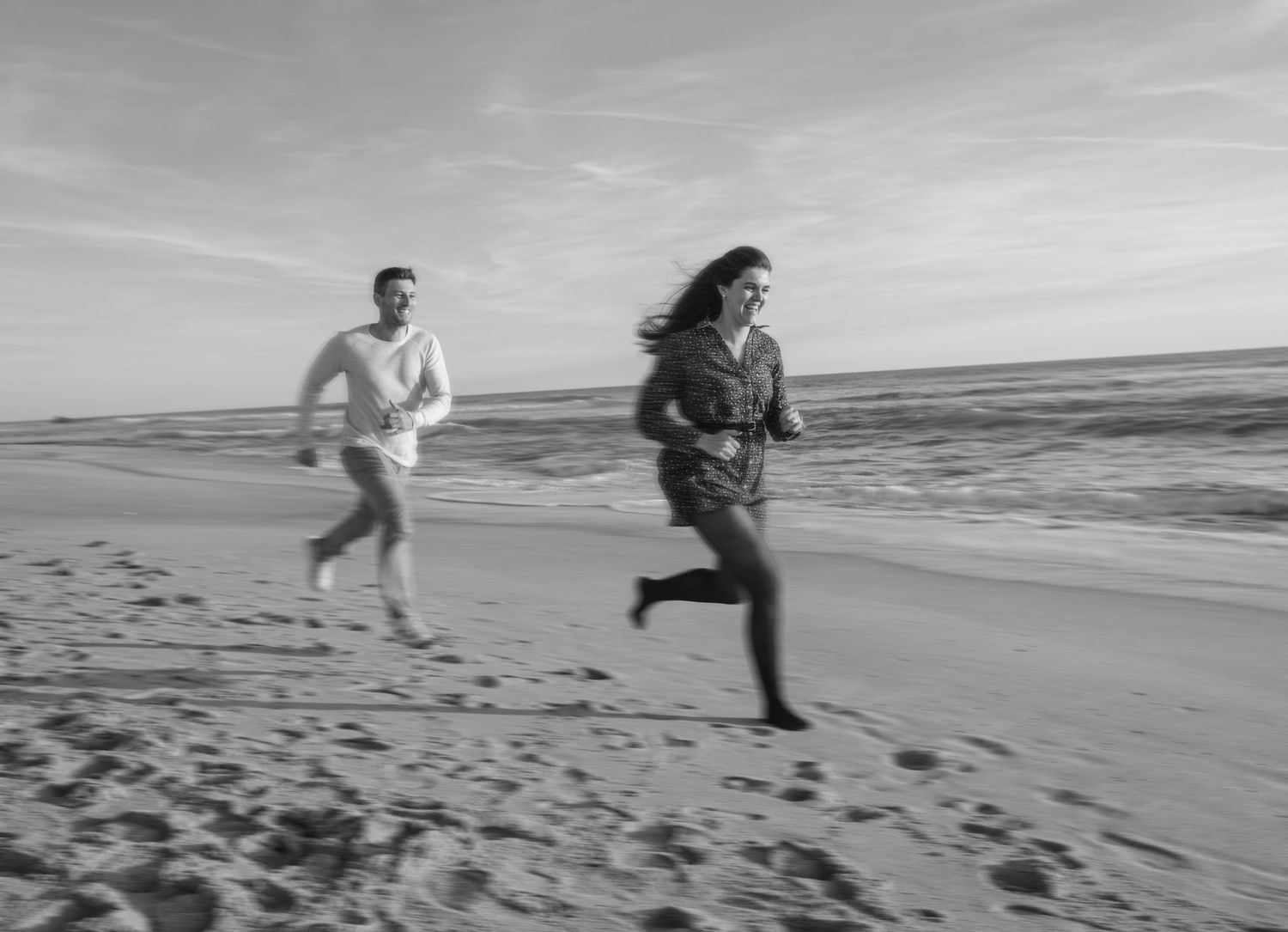 People run playfully along the beach shore in black and white.
