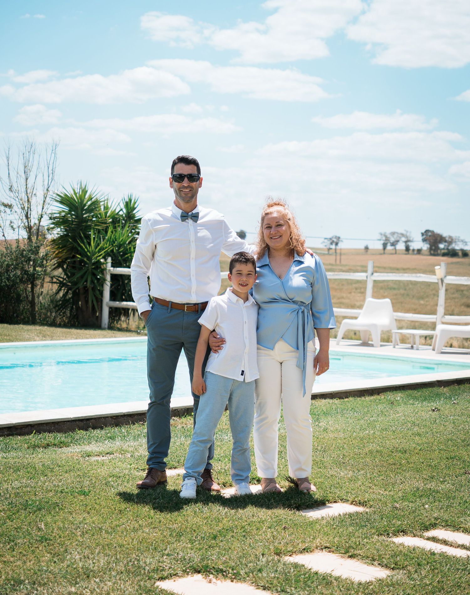 Outdoor gathering by a swimming pool on a sunny day with white fencing.