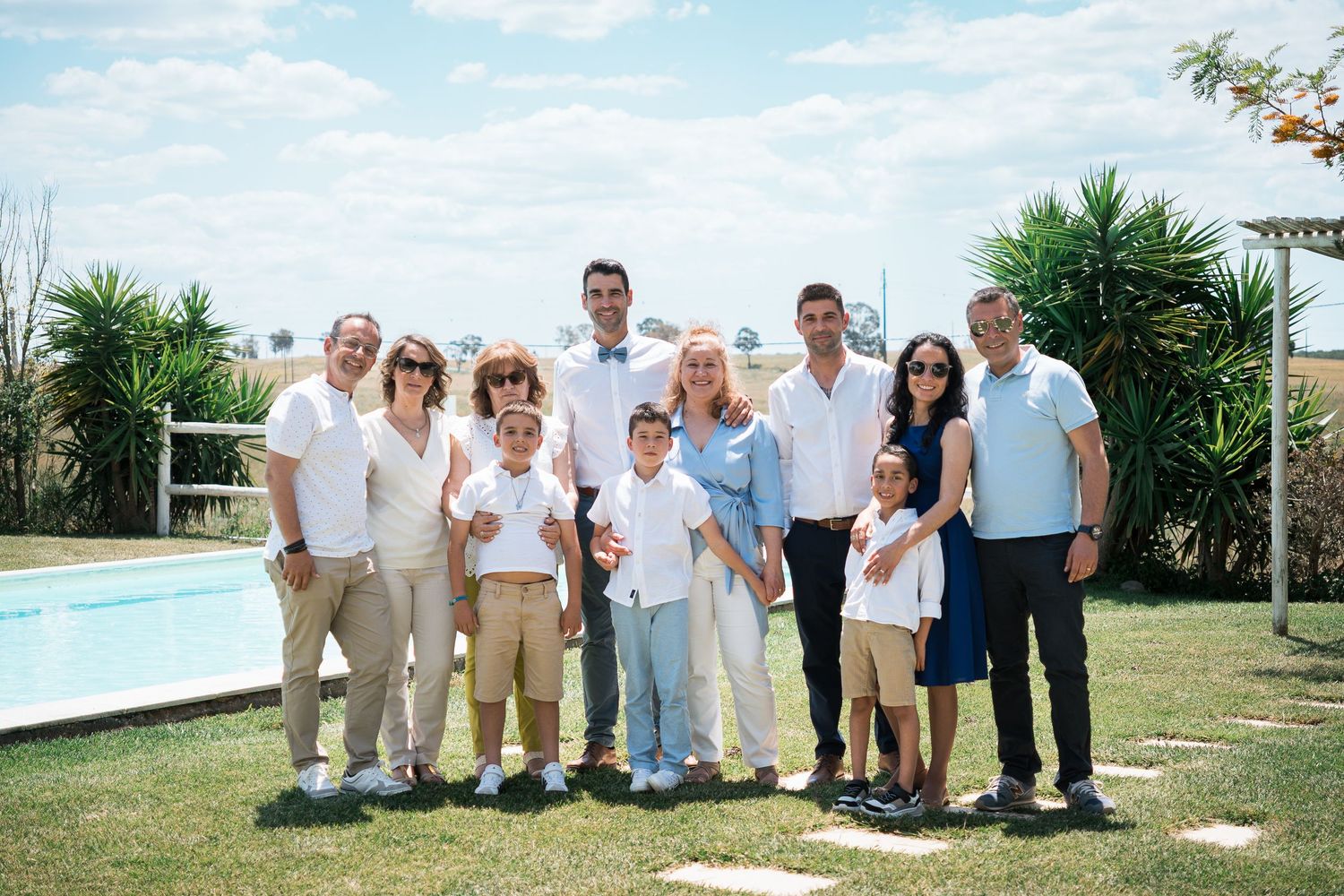 Large group portrait of wedding attendees gathered outdoors on a bright summer day.