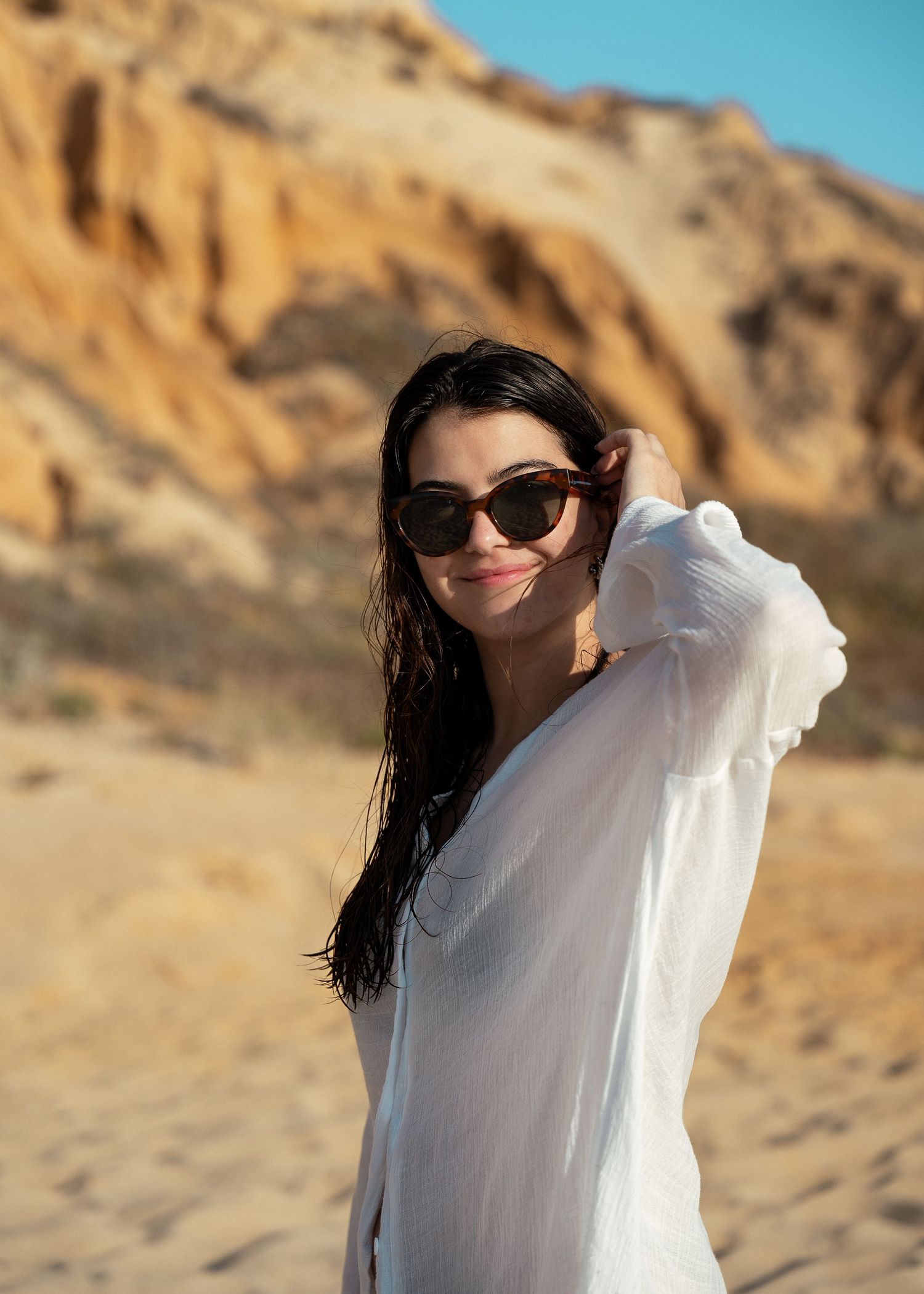 Person in white flowing cover-up posing against desert cliff backdrop.