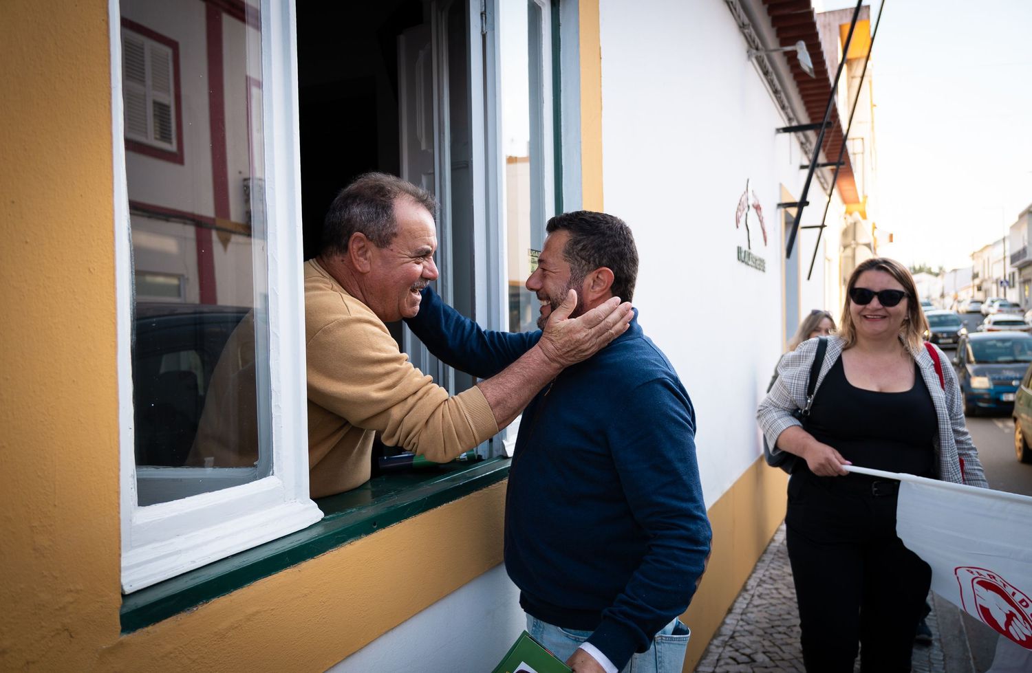 People interacting near yellow-painted building walls and windows in casual setting.