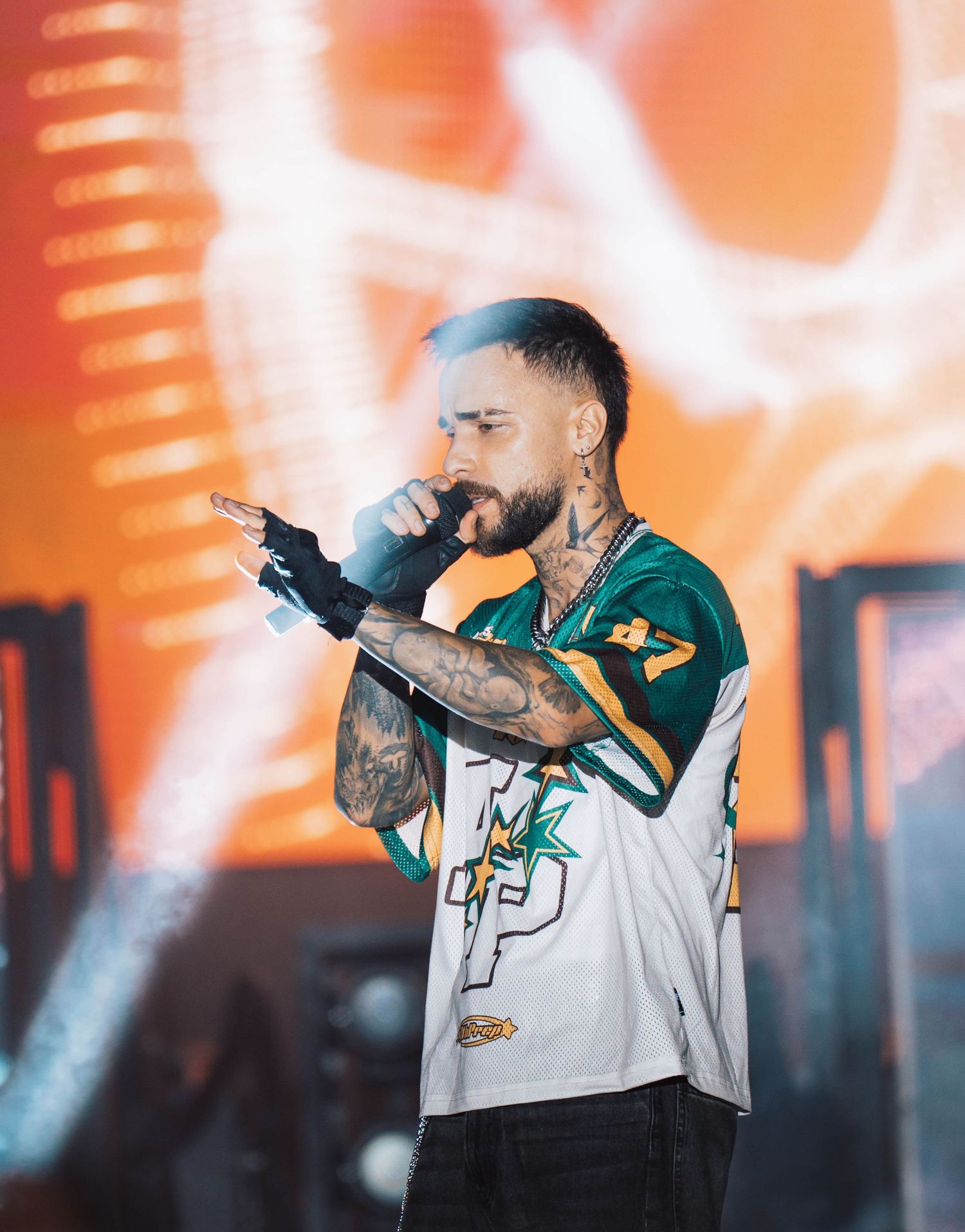 Artist performing on stage with orange lighting effects and wearing sports jersey.