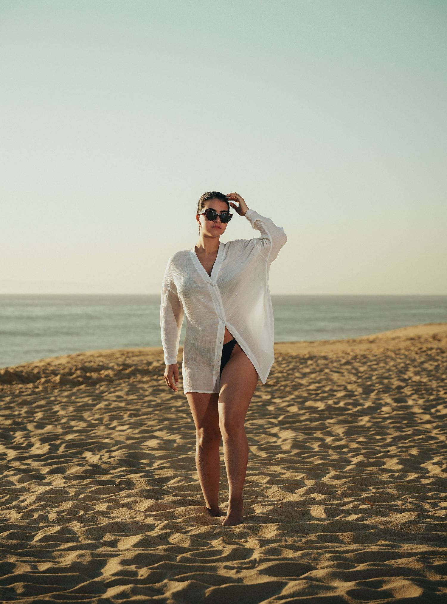 Woman in white shirt walking on sandy beach at sunset.