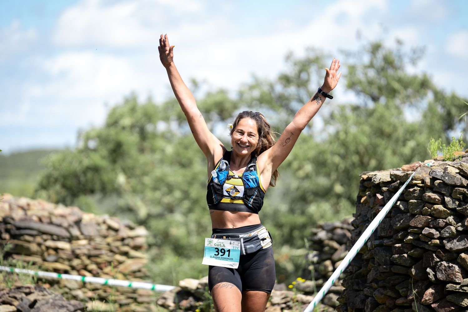 Athletes celebrating at finish line with arms raised against stone wall backdrop.