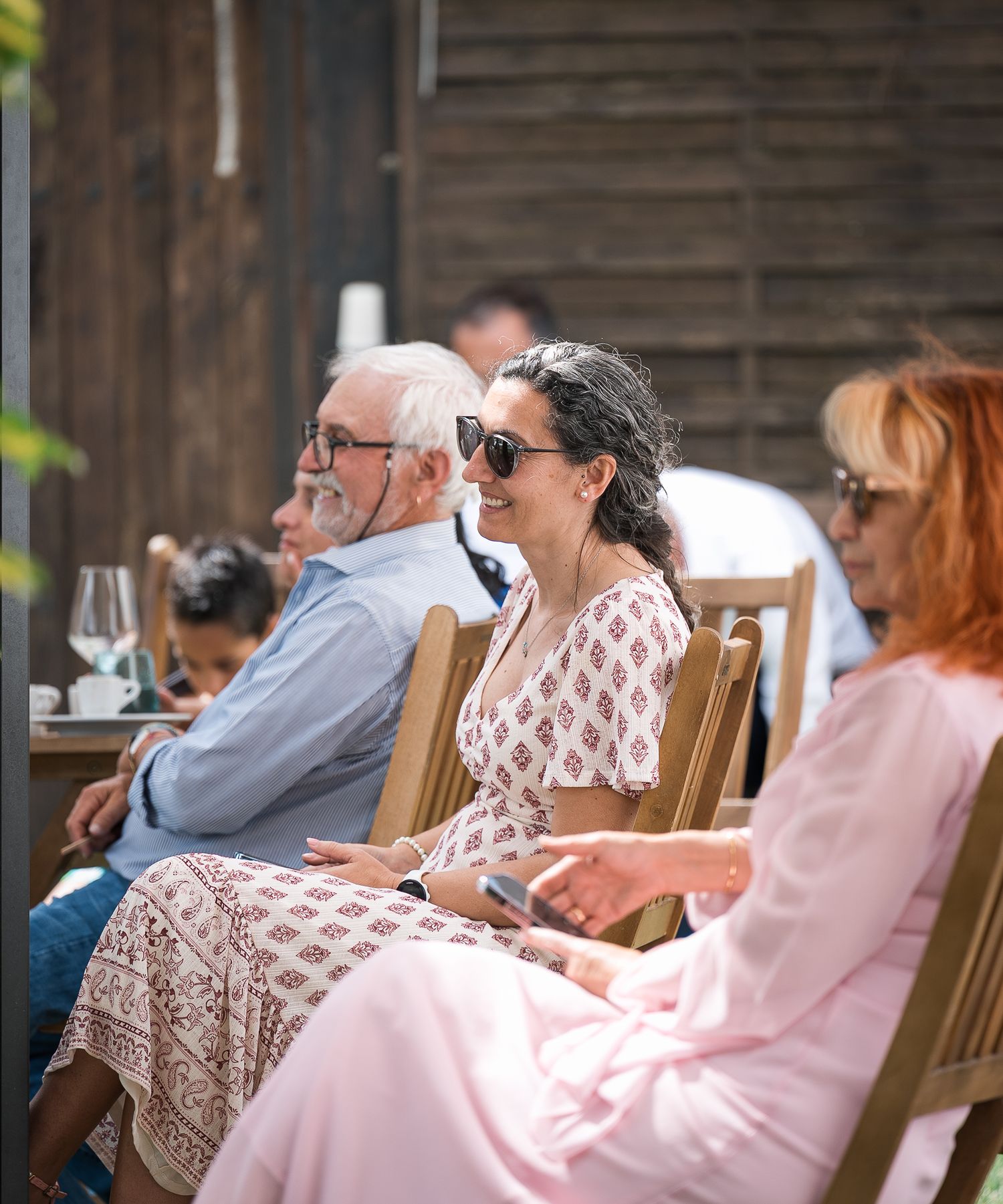 Wedding guests relaxing in wooden chairs during outdoor reception.