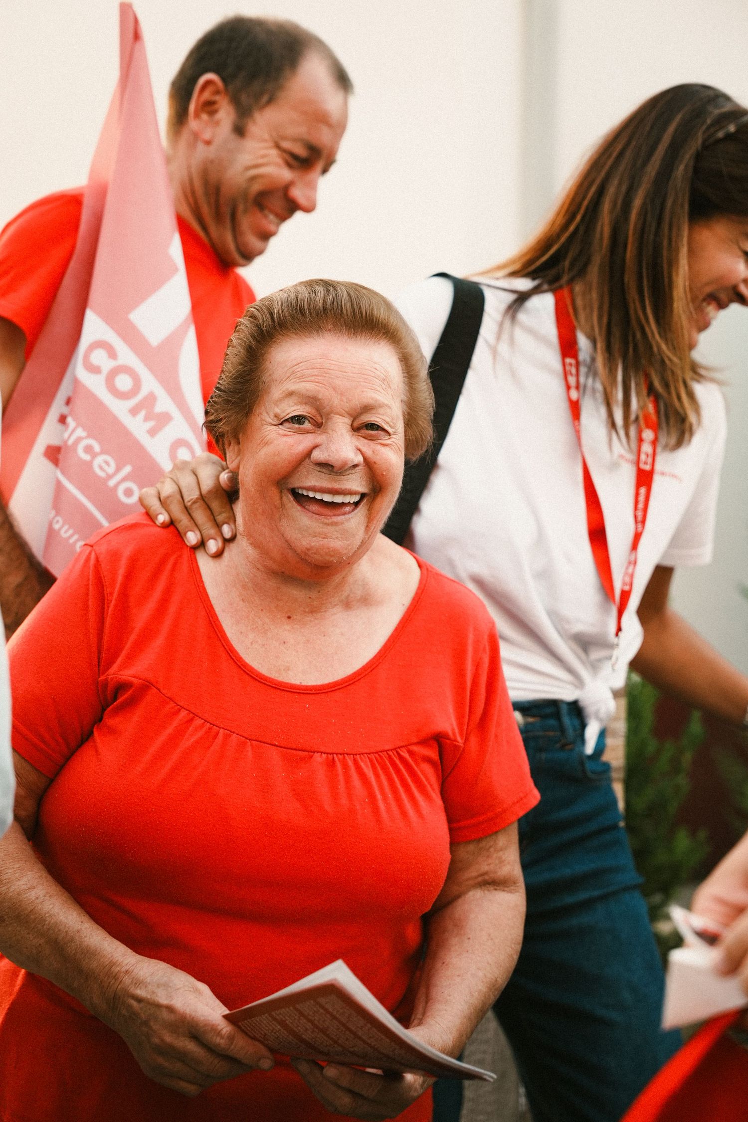 People in red and white attire sharing warm smiles and embraces at a community event.