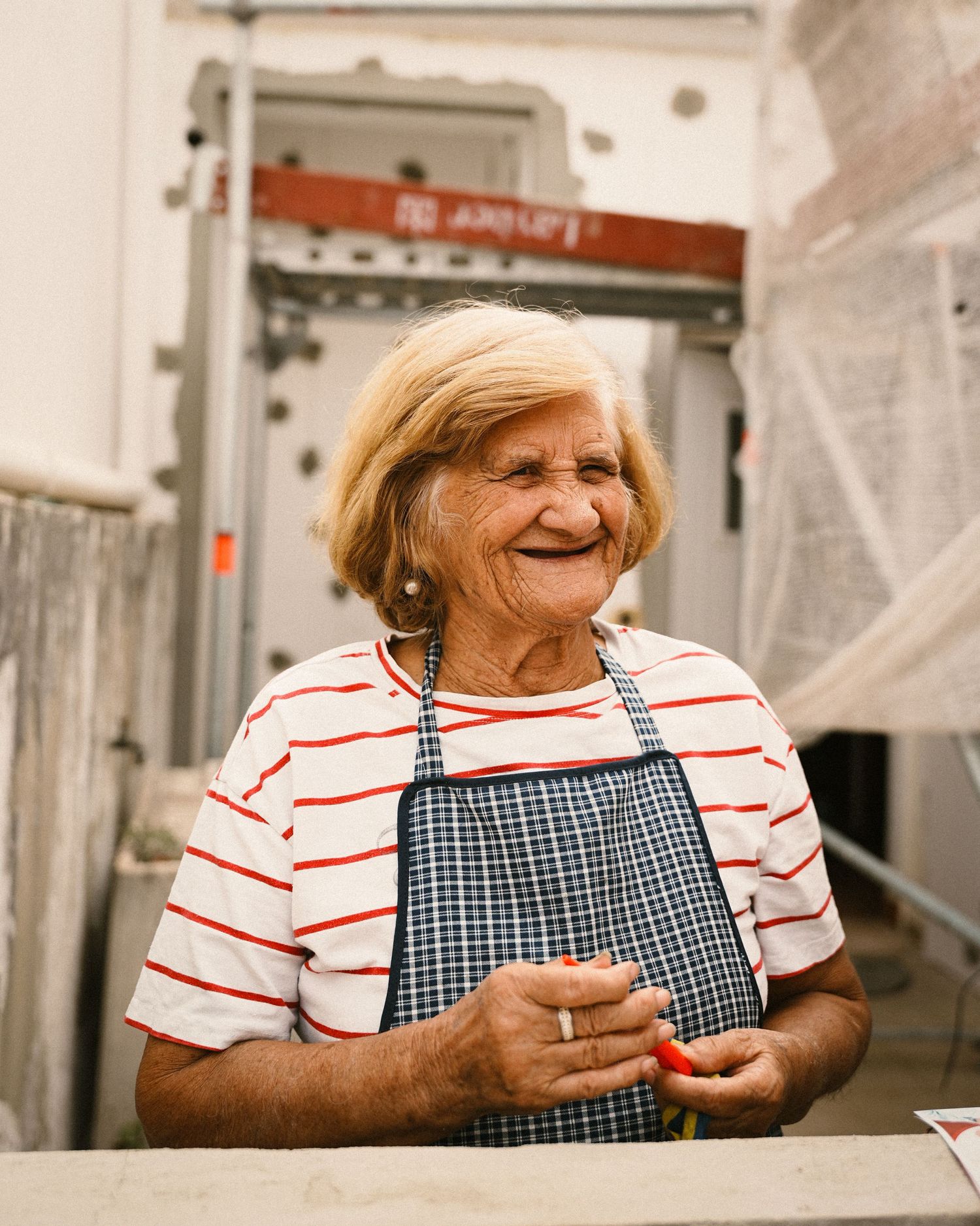 Person in striped shirt and checkered apron looking to the side indoors.