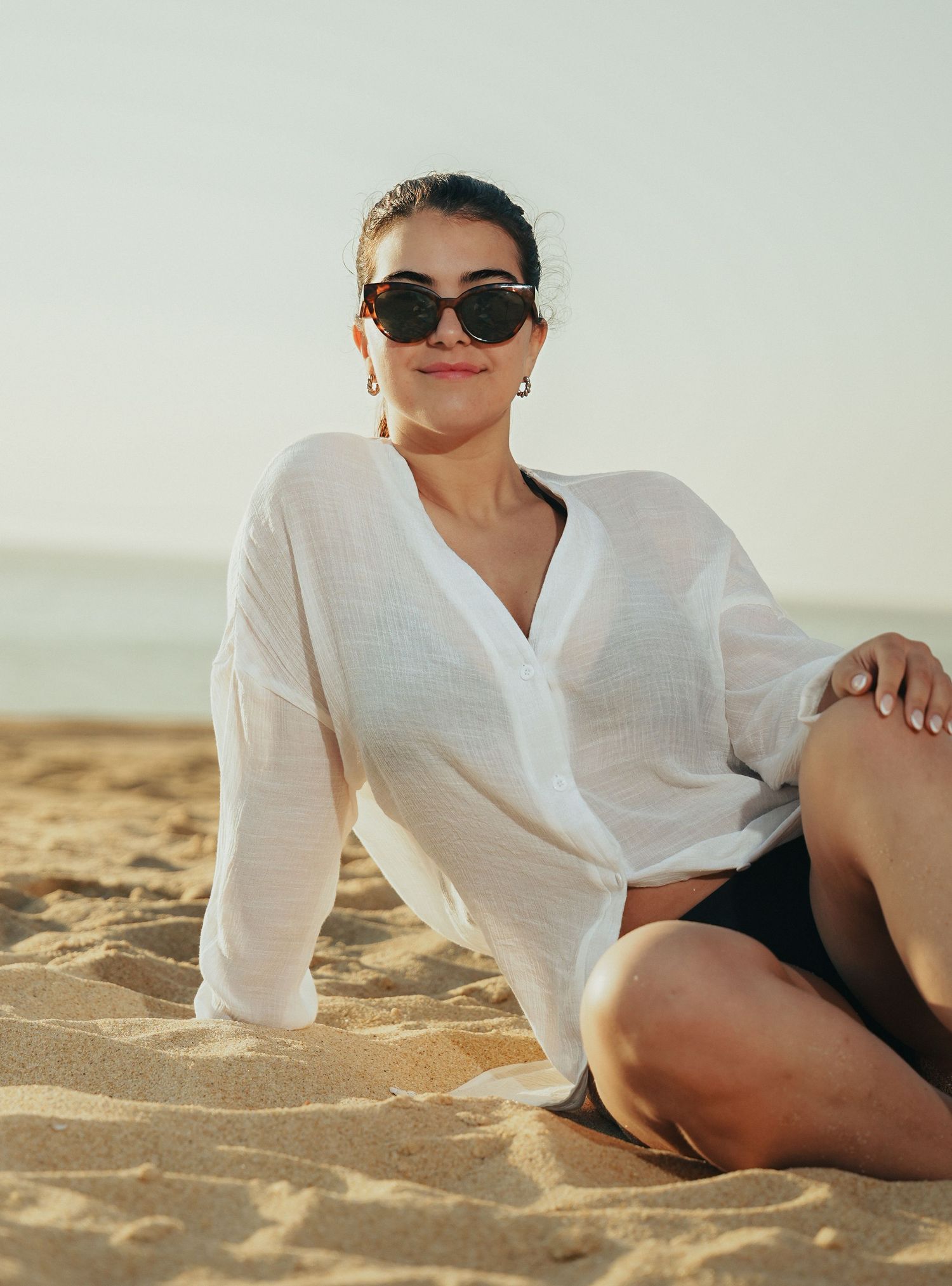 Person in white shirt lounging on sandy beach during golden hour.