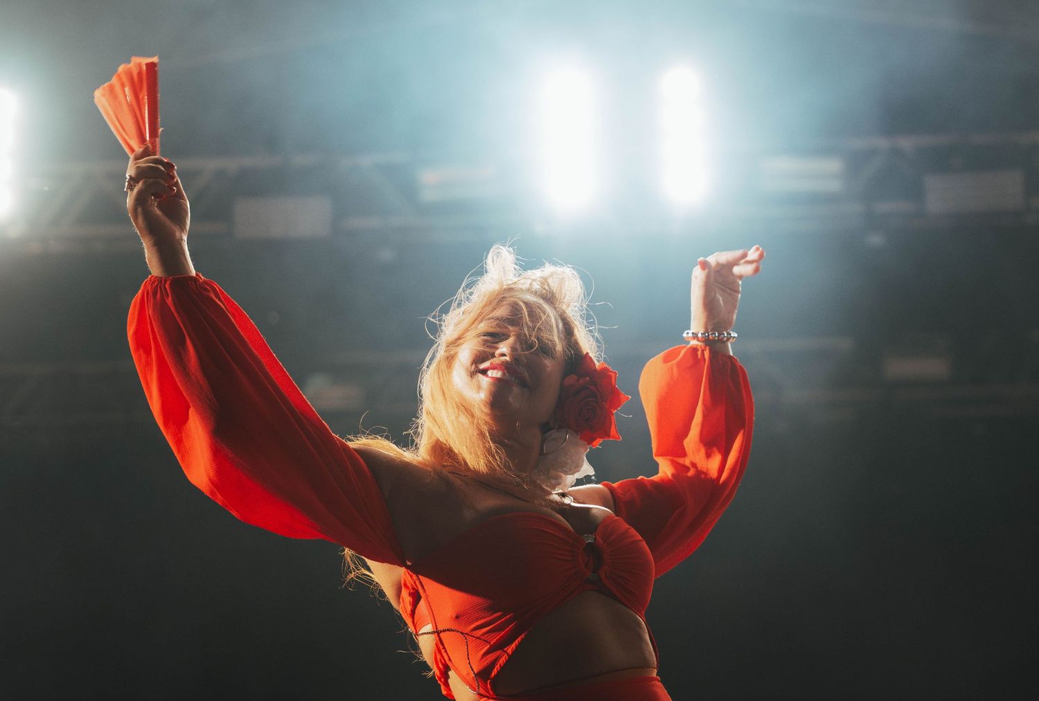 Performers in black outfits moving dynamically on stage with bright orange lighting effects.