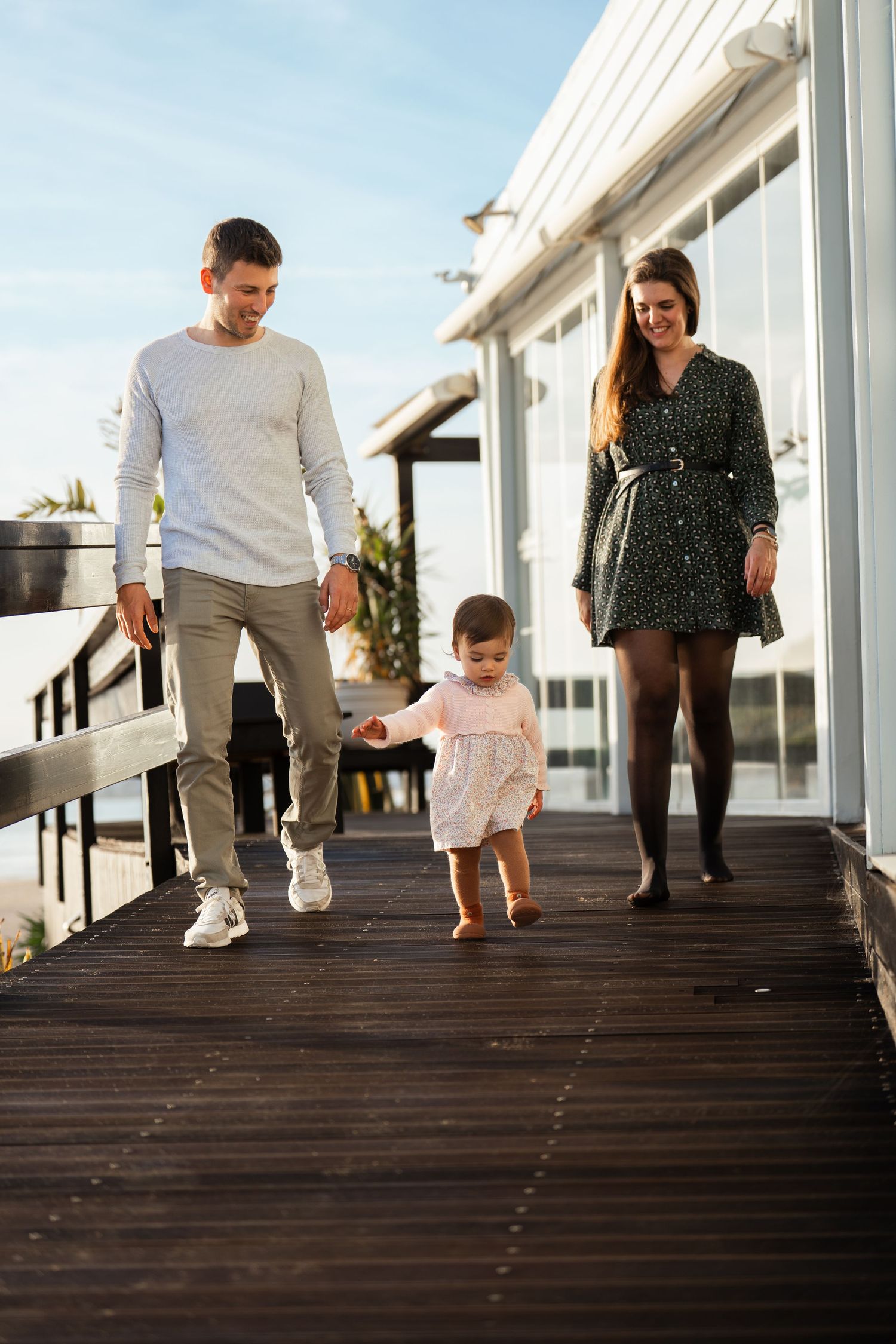 Family walking together on a wooden boardwalk near the beach on a sunny day.