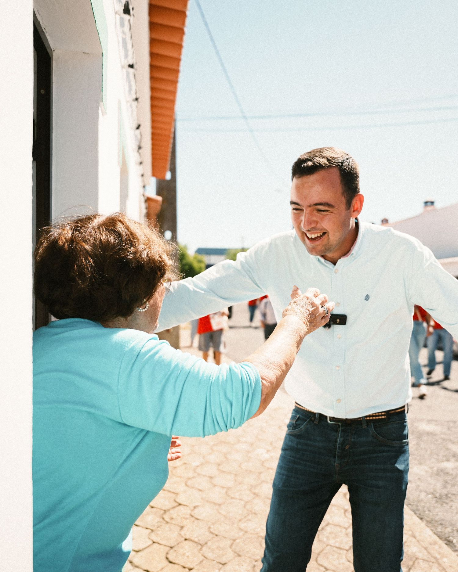 People engaged in playful interaction outside a white building under bright sunlight.