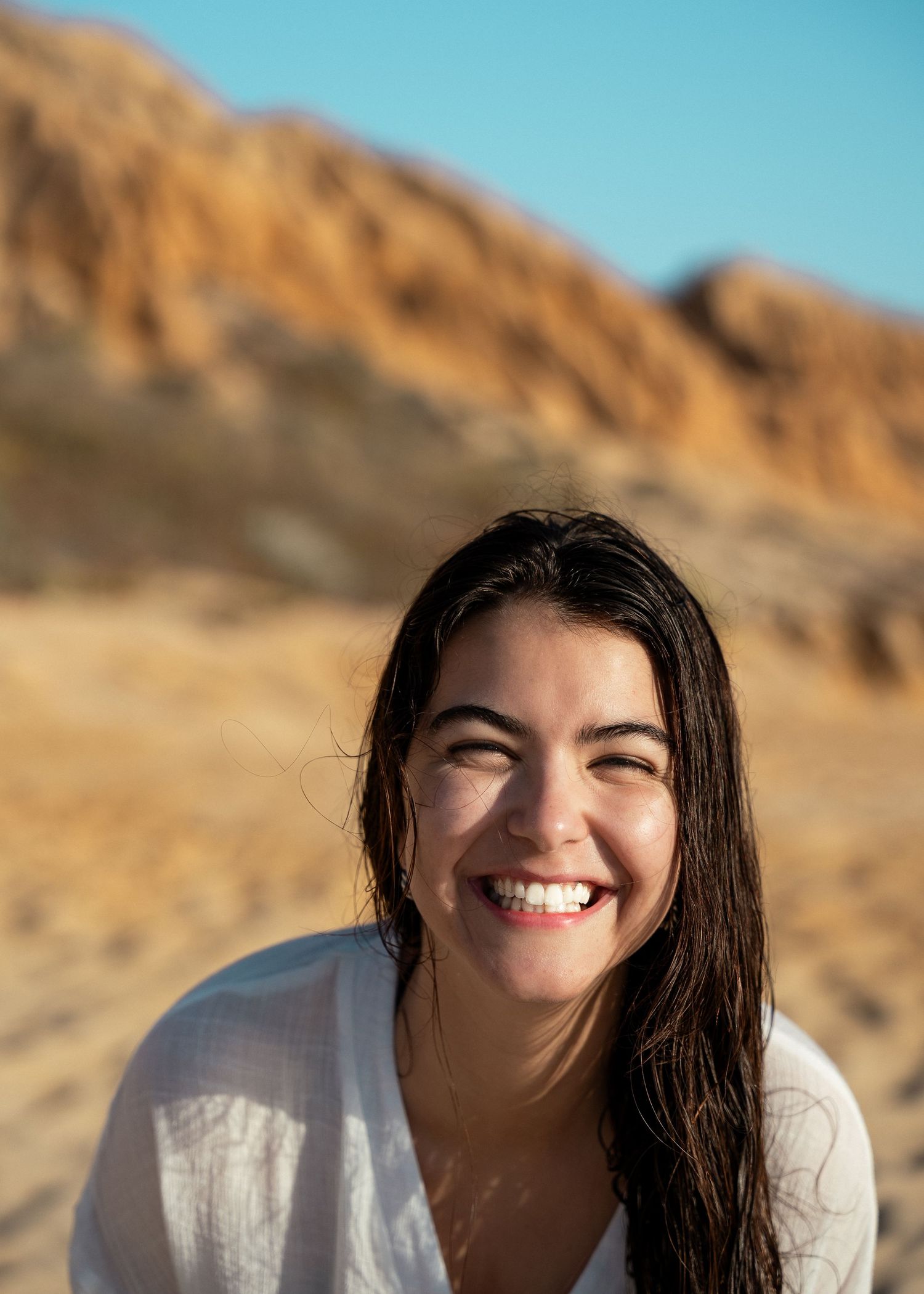 Woman in white shirt smiling and laughing while posing against desert mountain backdrop.
