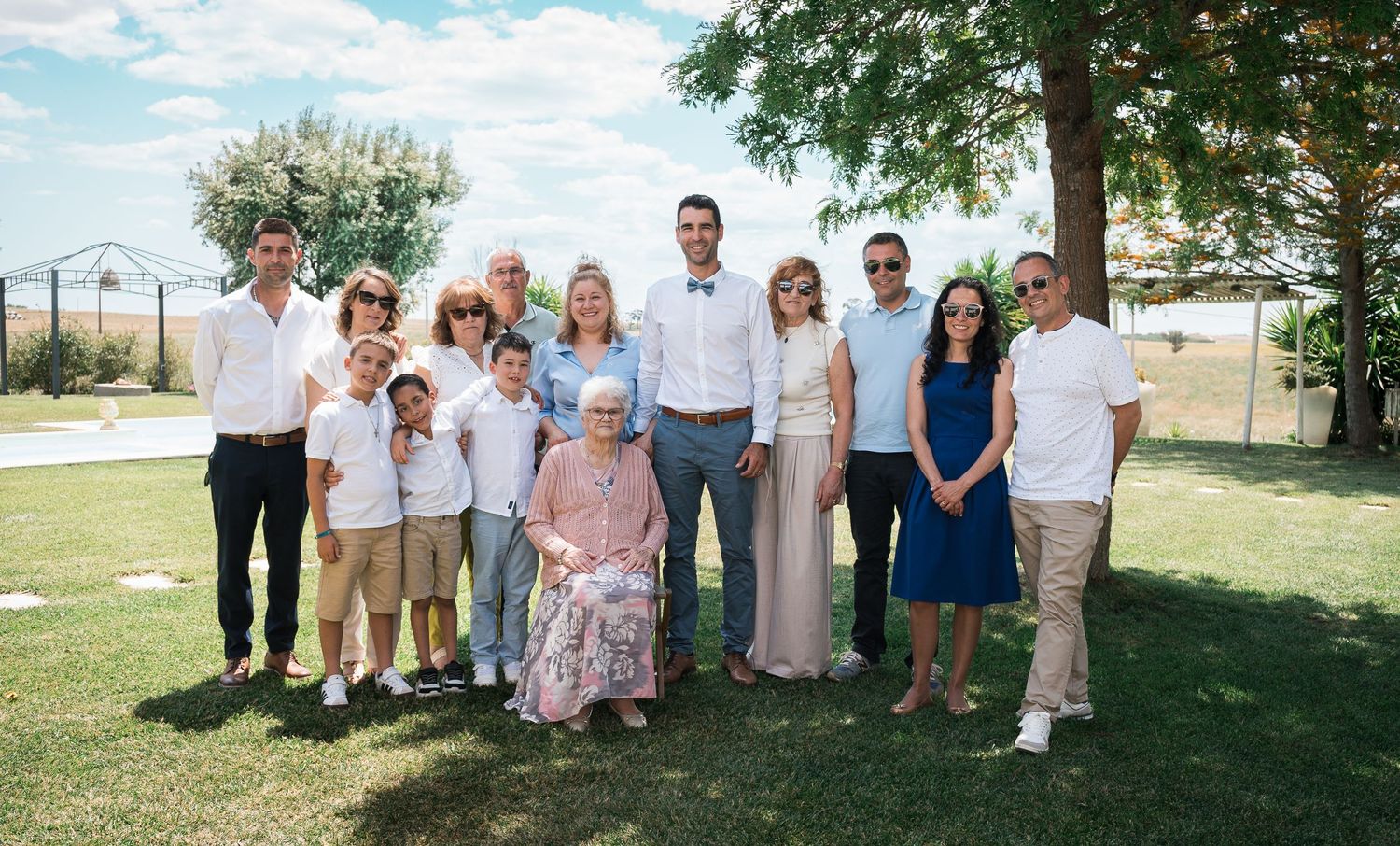 Wedding party and guests lined up for a panoramic photo outdoors under blue skies.
