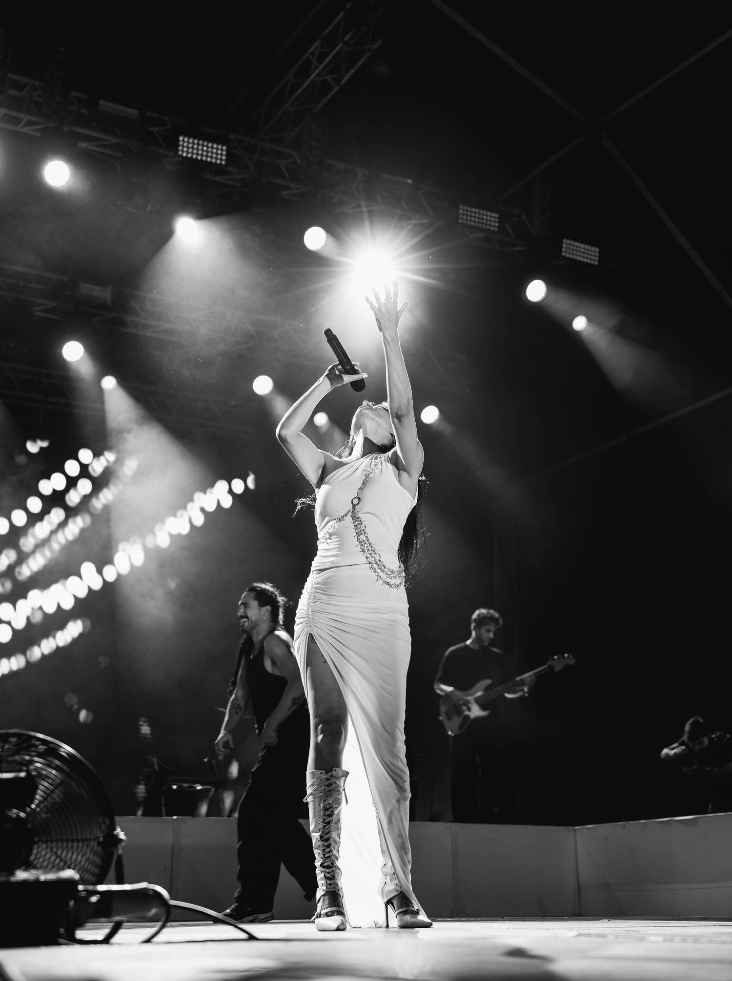 Dramatic black and white performance shot on stage with theatrical lighting.
