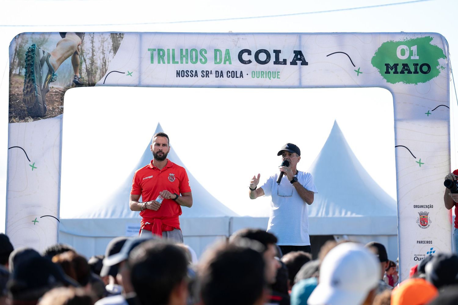 Two speakers on stage at Trilhos da Cola outdoor running event.