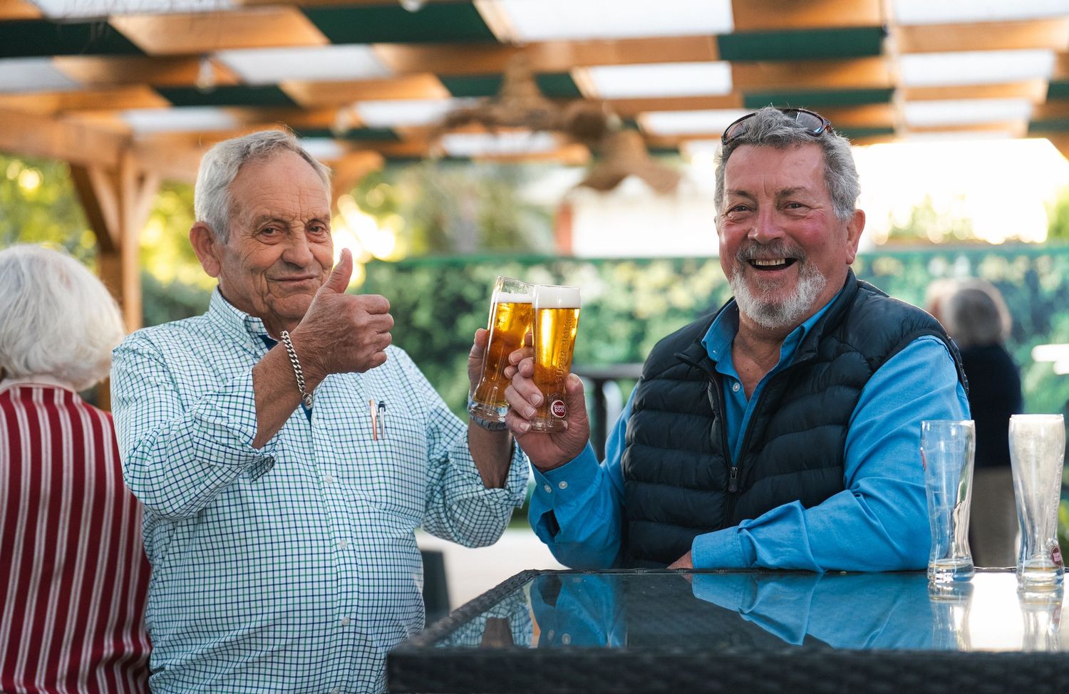 Group enjoying conversation and drinks at an outdoor gathering with wooden beams overhead.