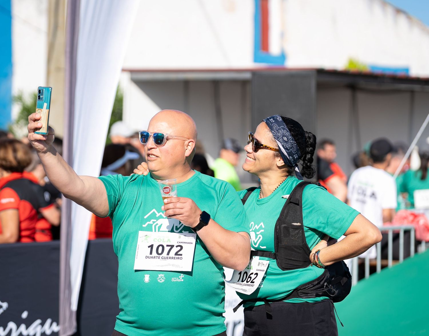 Two participants in matching green shirts take a selfie during a running event.