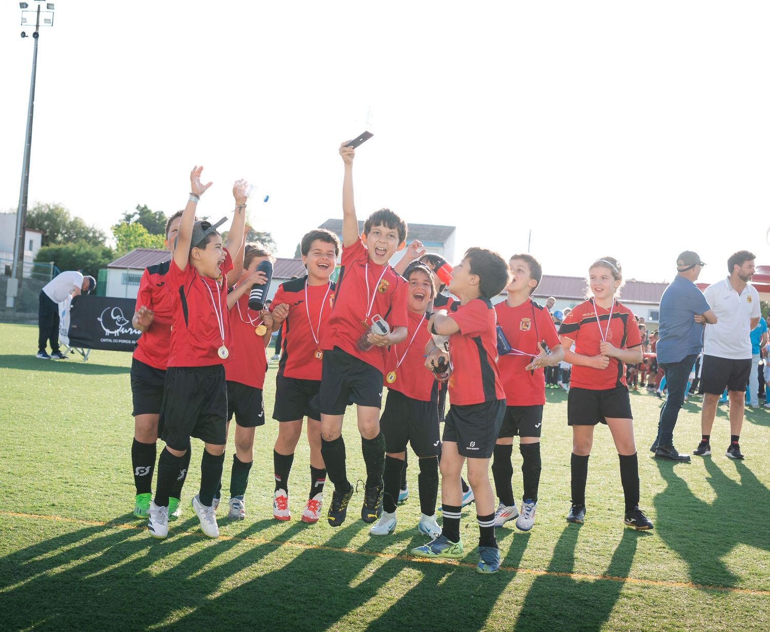 Youth soccer team lined up on field with arms raised celebrating together.