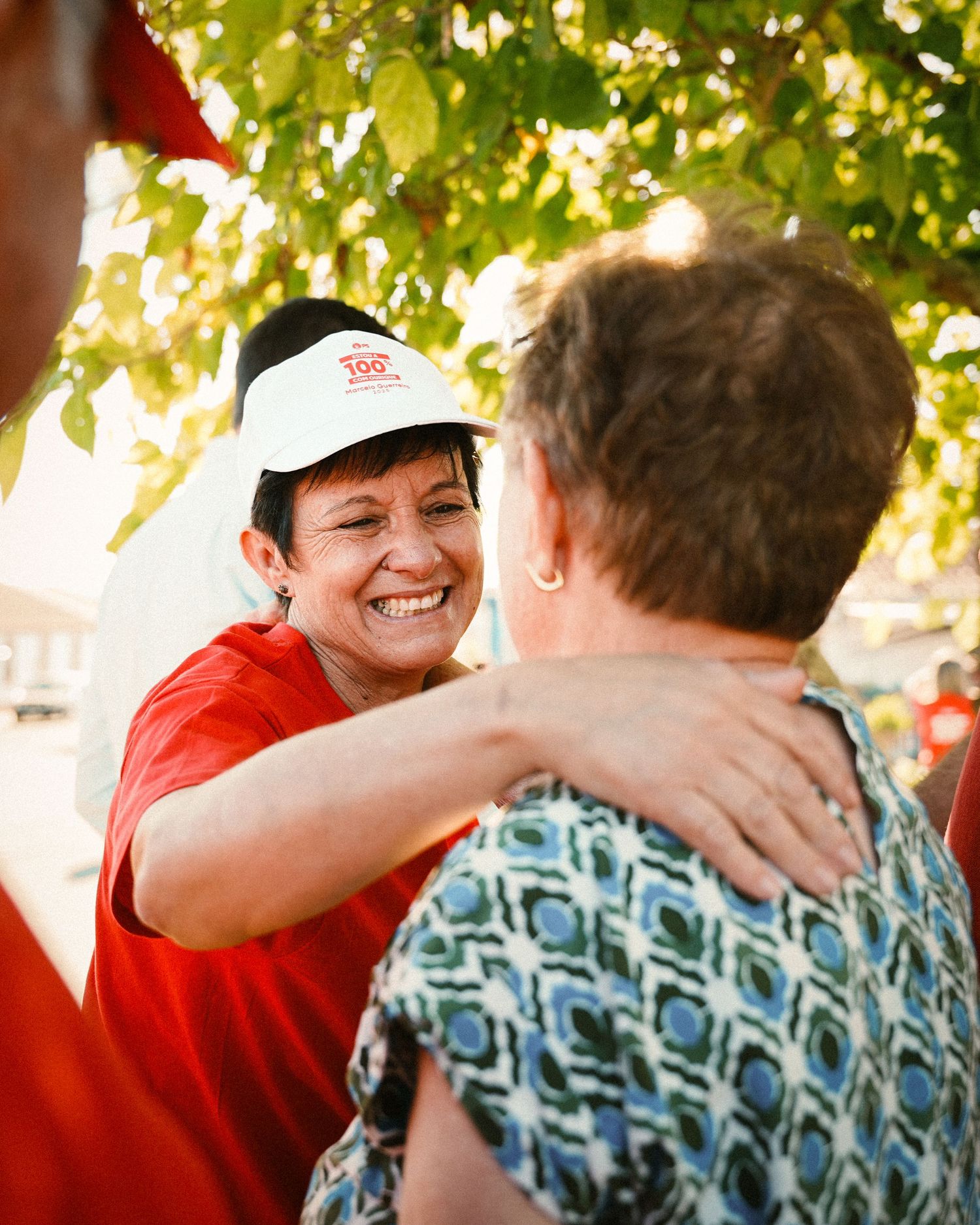 Casual gathering under trees with people wearing red shirts and patterned clothing.