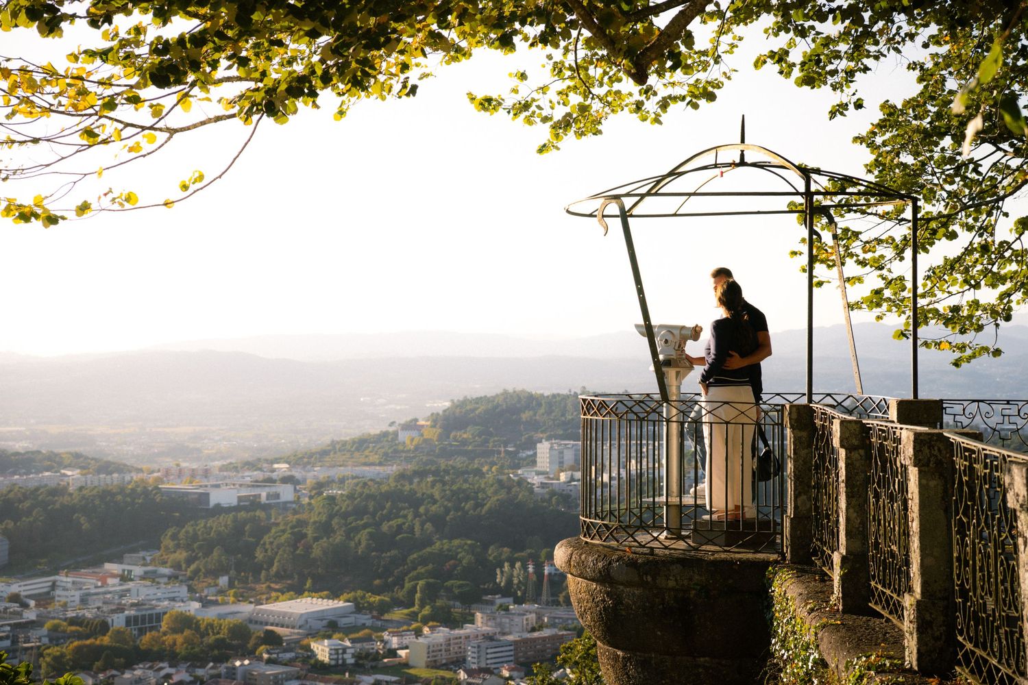 Scenic mountain overlook with trees framing panoramic city view.