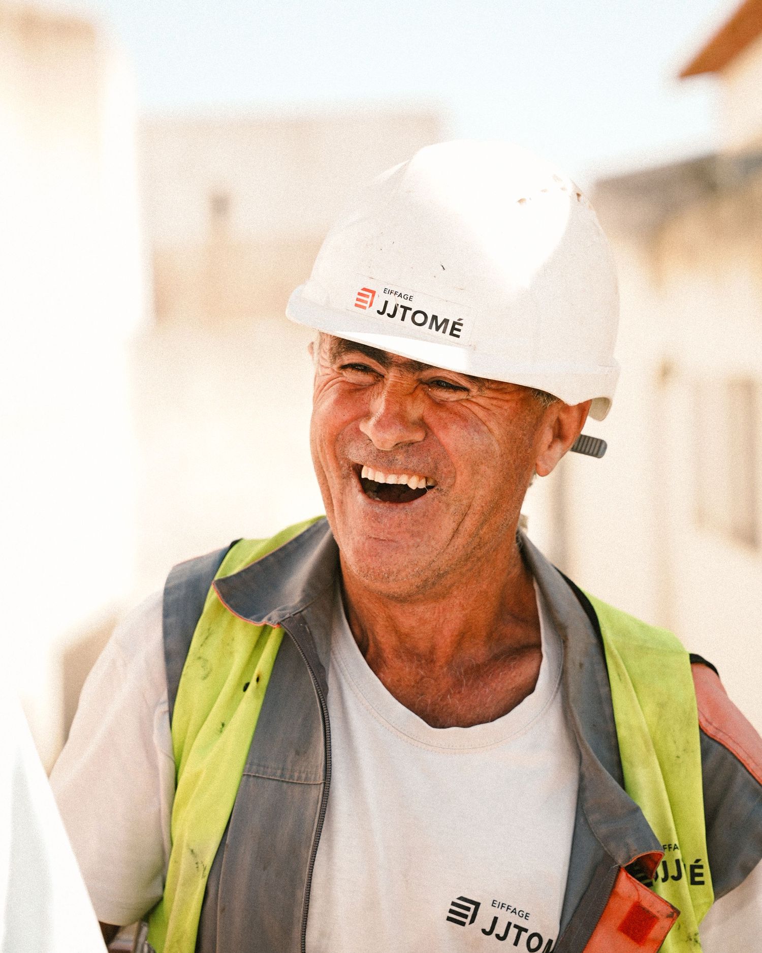 Construction worker in safety gear and white hard hat smiles warmly outdoors.