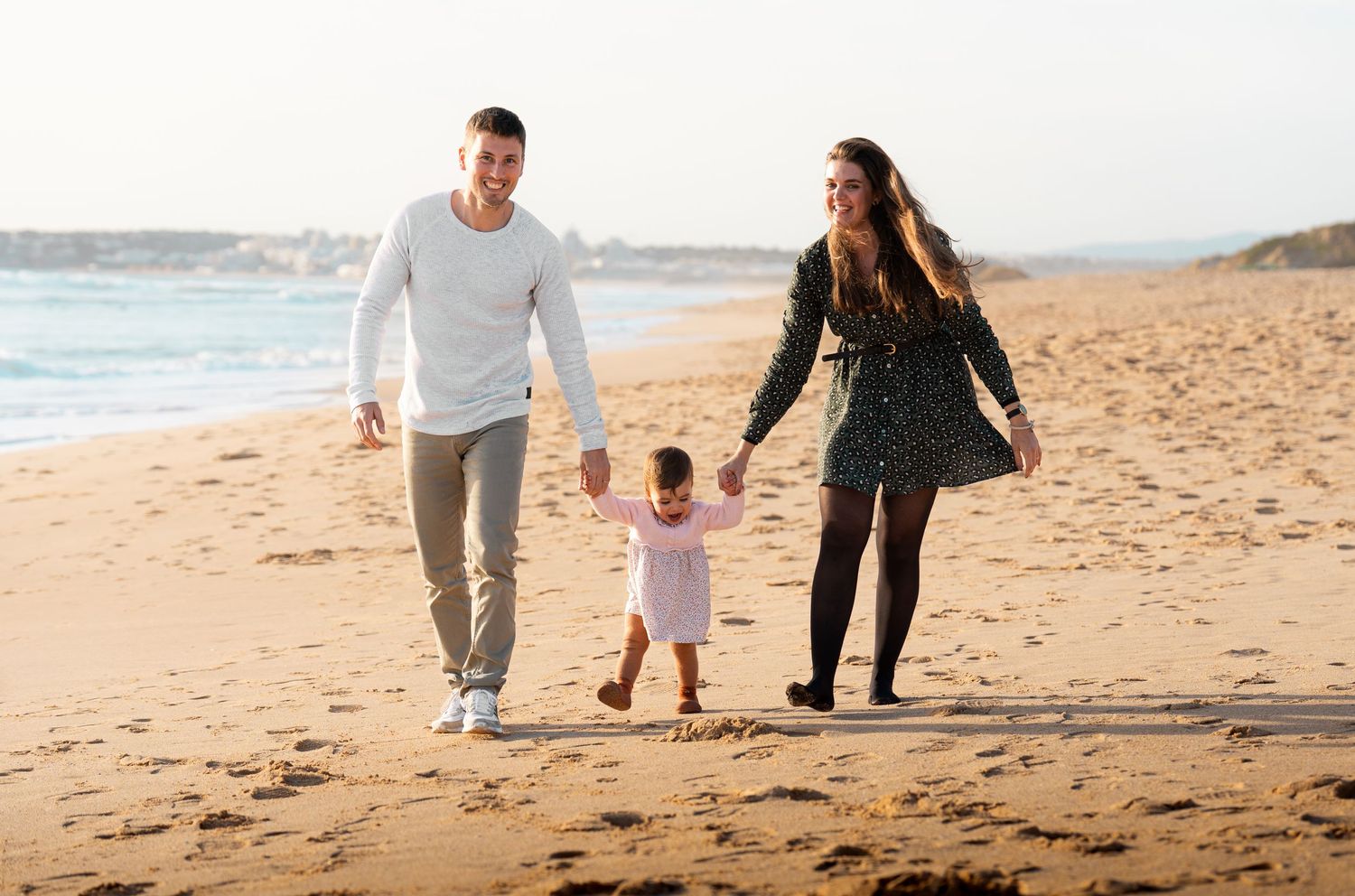 A family walks hand in hand along a scenic beach at sunset.