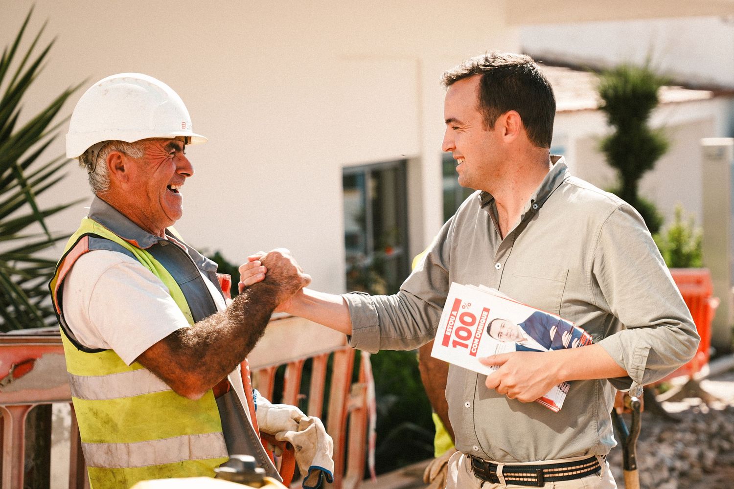 Construction worker and business professional shake hands at outdoor worksite.