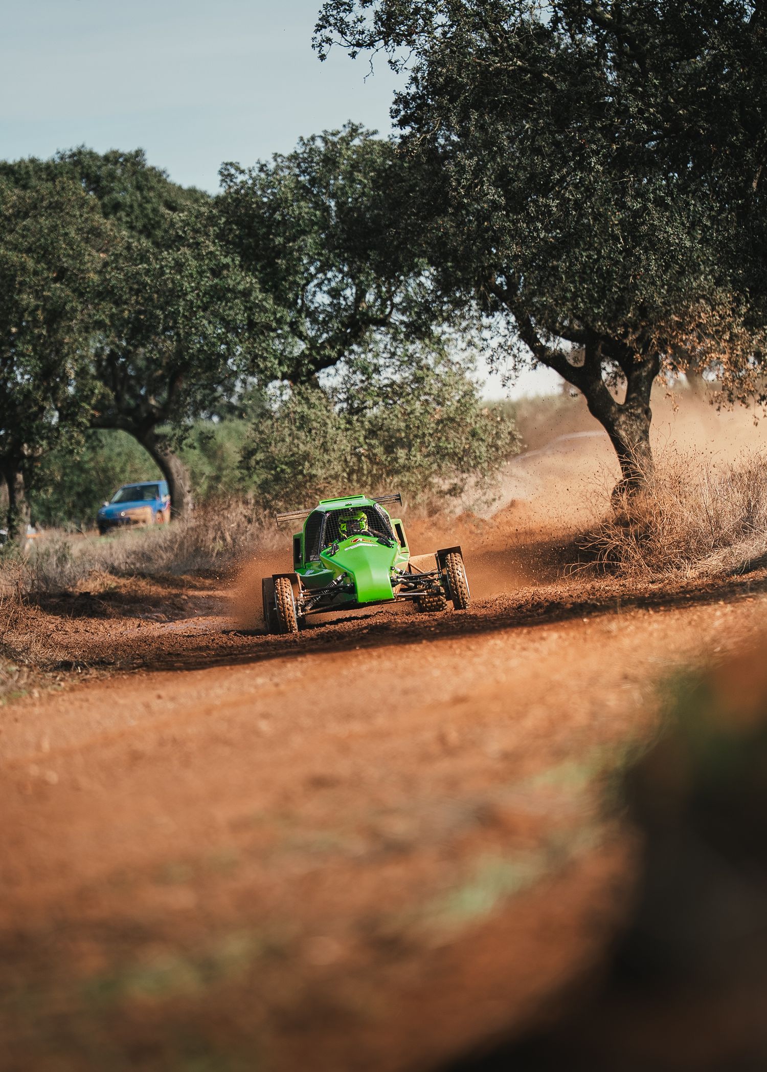 Low angle shot of an off-road vehicle speeding through a dirt course surrounded by oak trees.