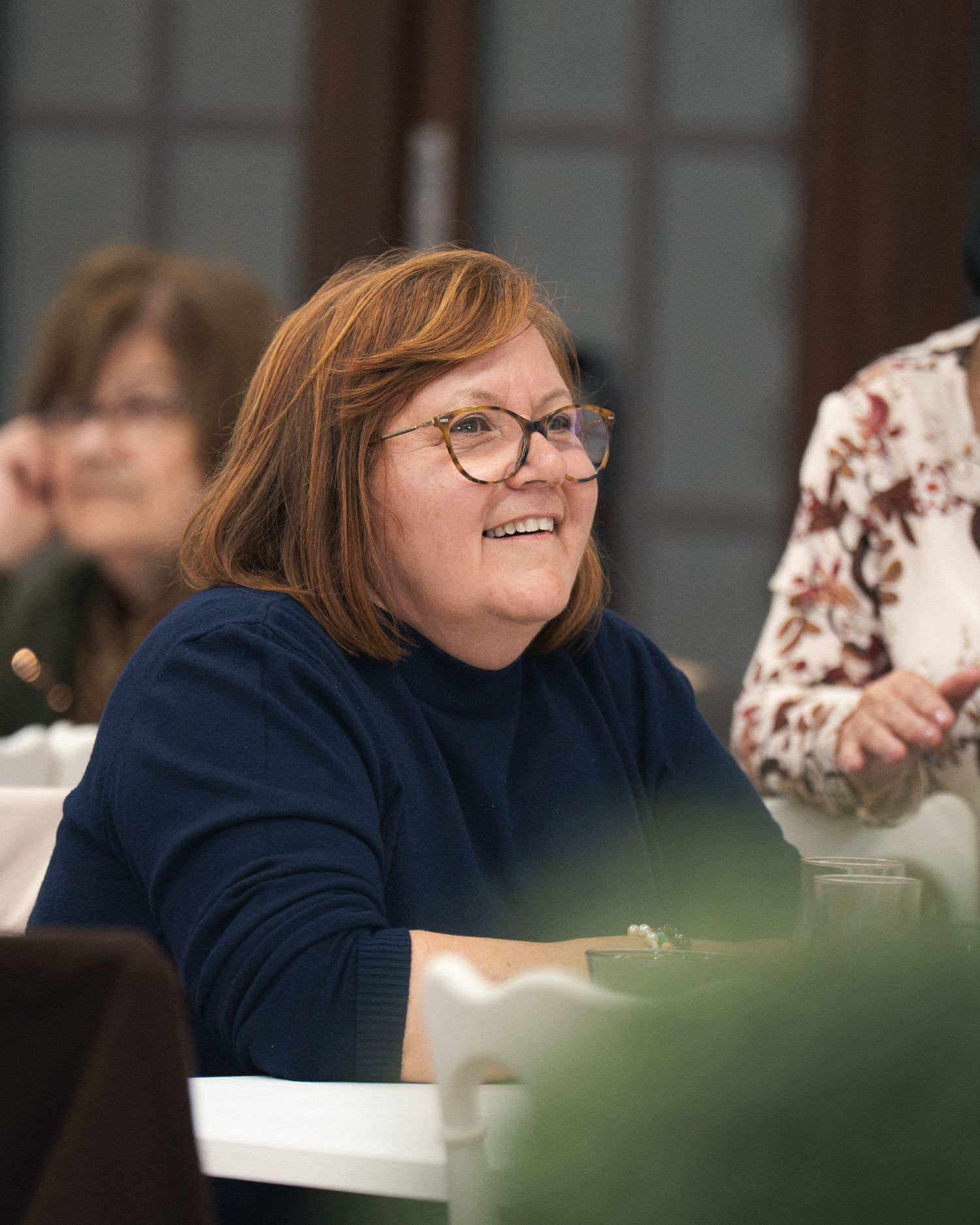 Person in navy sweater smiling and gesturing animatedly during a group conversation.