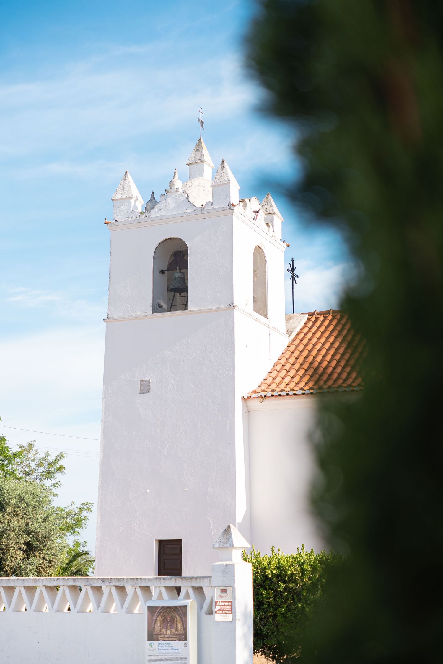 White church bell tower with terracotta roof tiles against blue sky in Mediterranean architectural style.