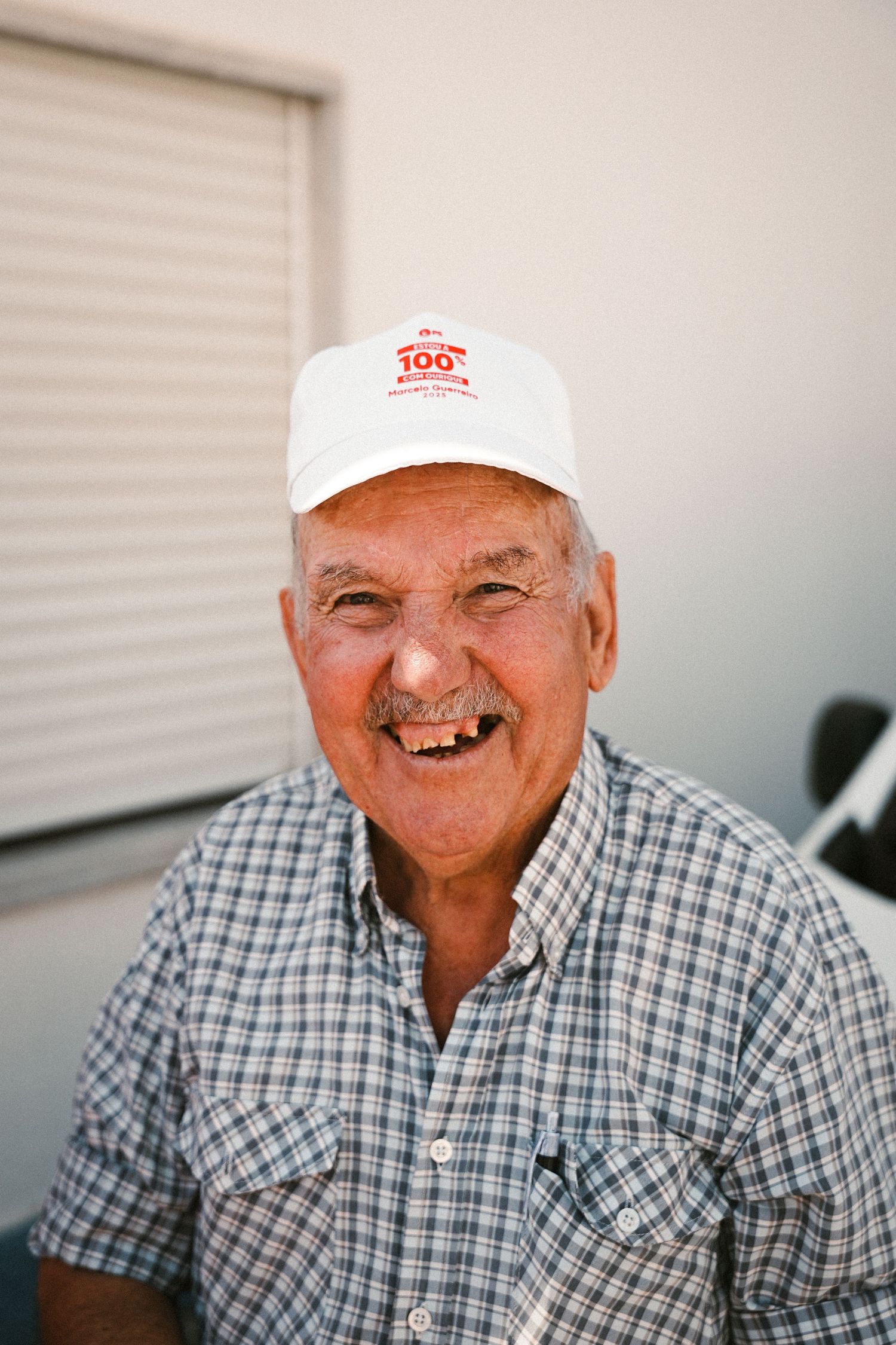 Person in plaid shirt and white cap smiling outdoors.
