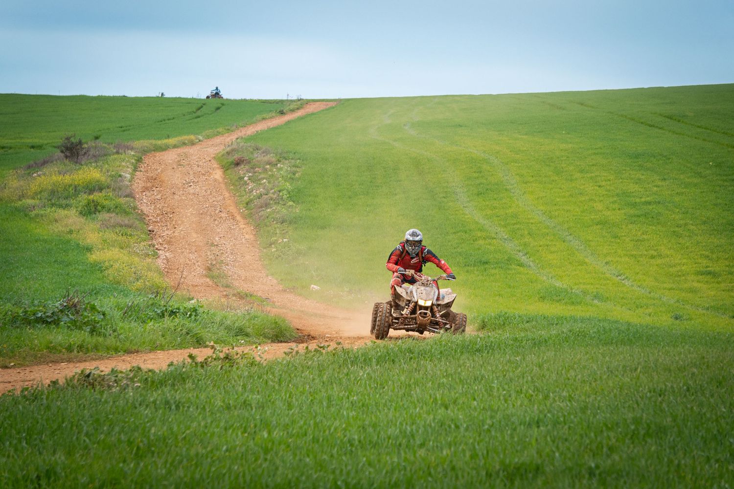 A dirt road winds through vibrant green rolling hills with a tractor visible in the distance.