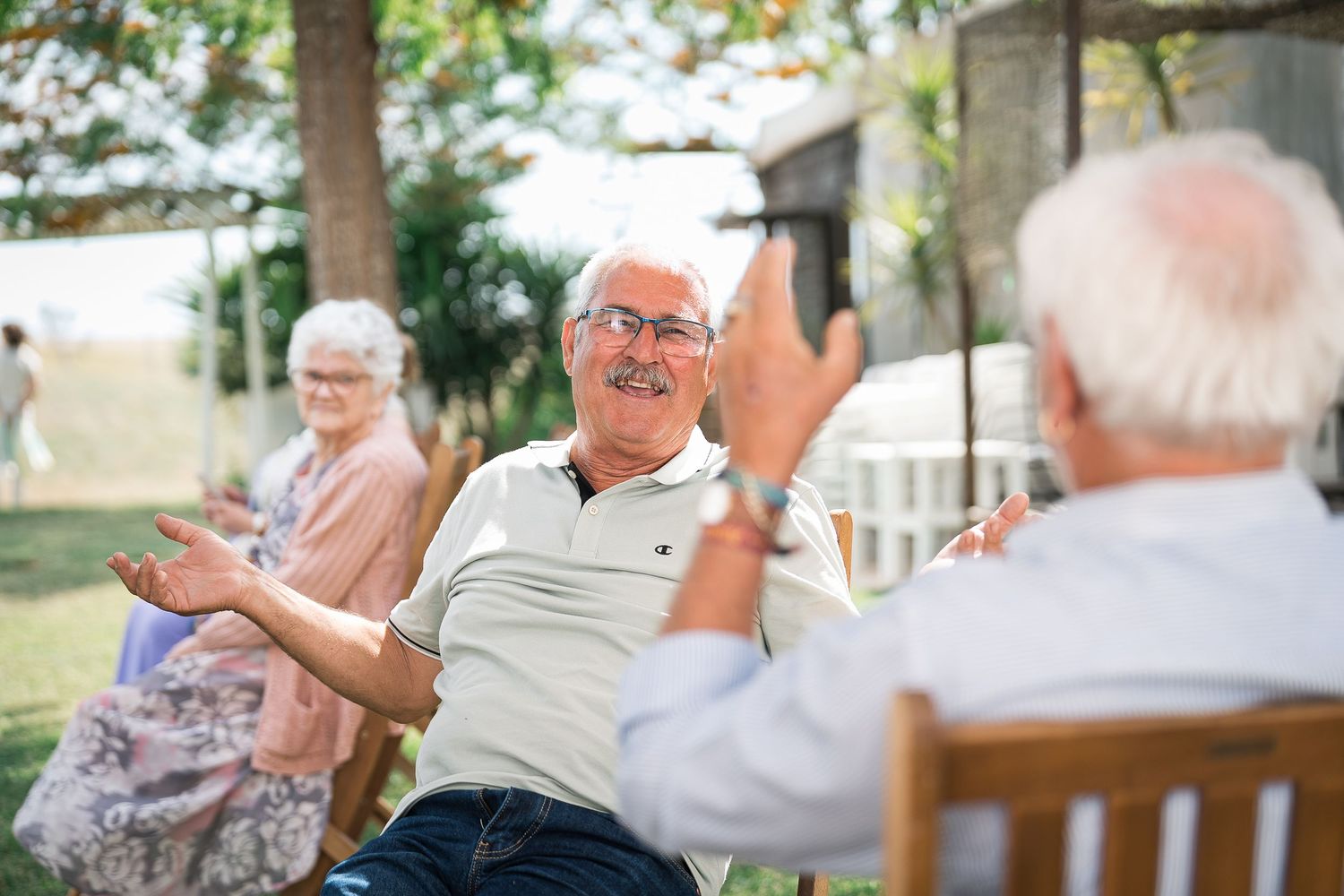 Group enjoying animated conversation while sitting outdoors in garden chairs.